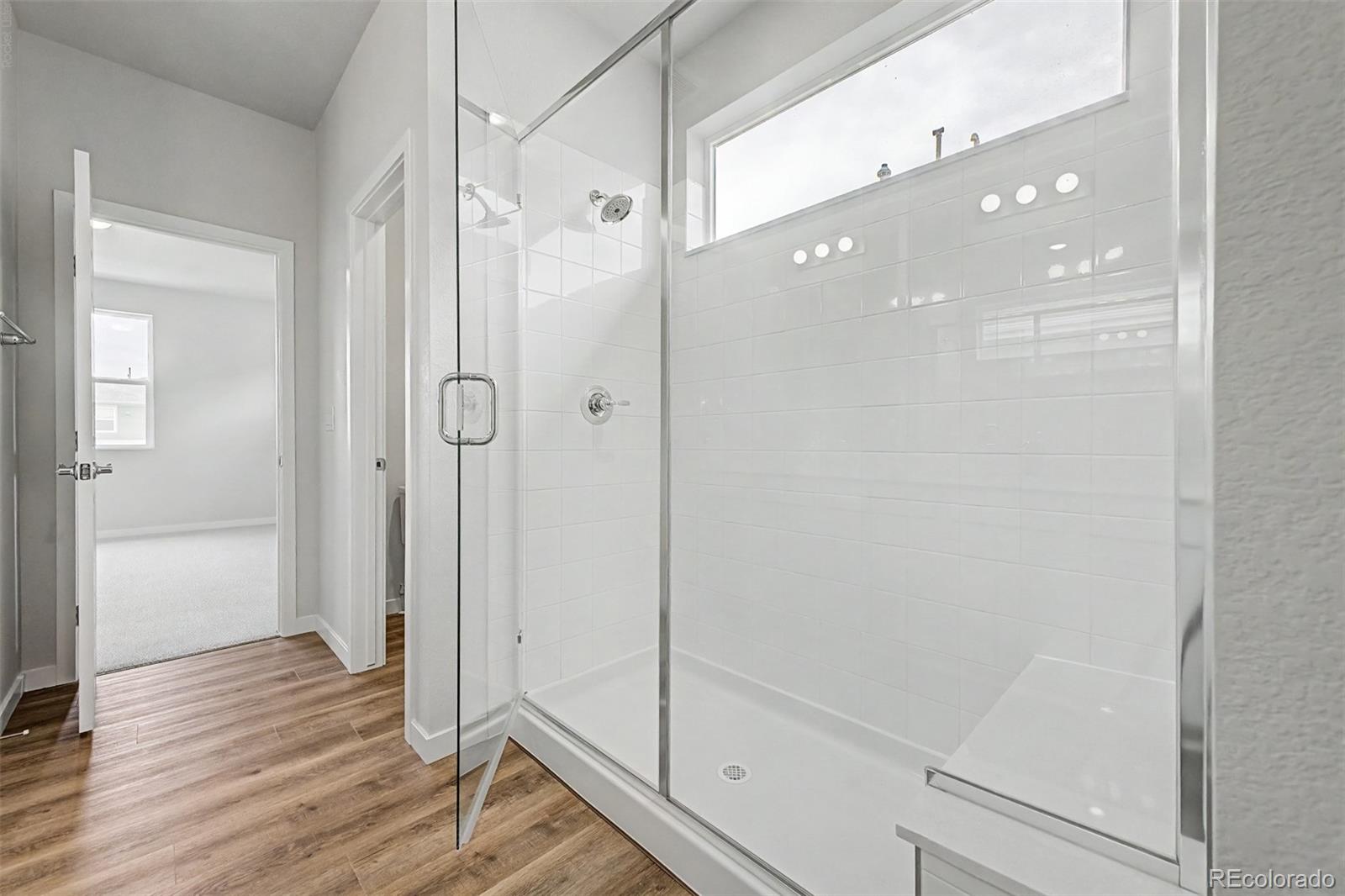 Bathroom with a glass-enclosed tiled shower, built-in bench, and high window.