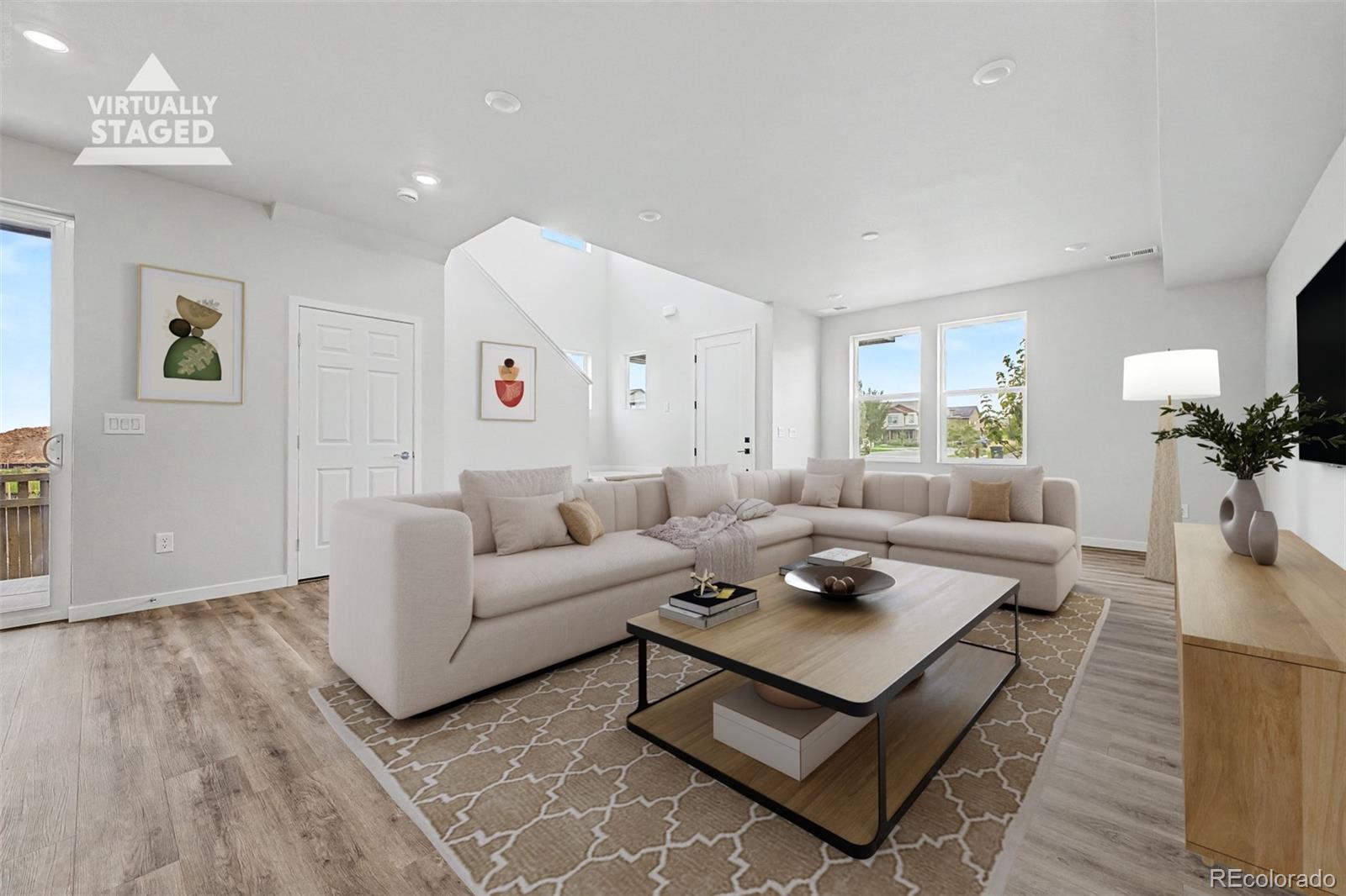 Virtually staged living room with a cream sectional, patterned rug, and bright windows.