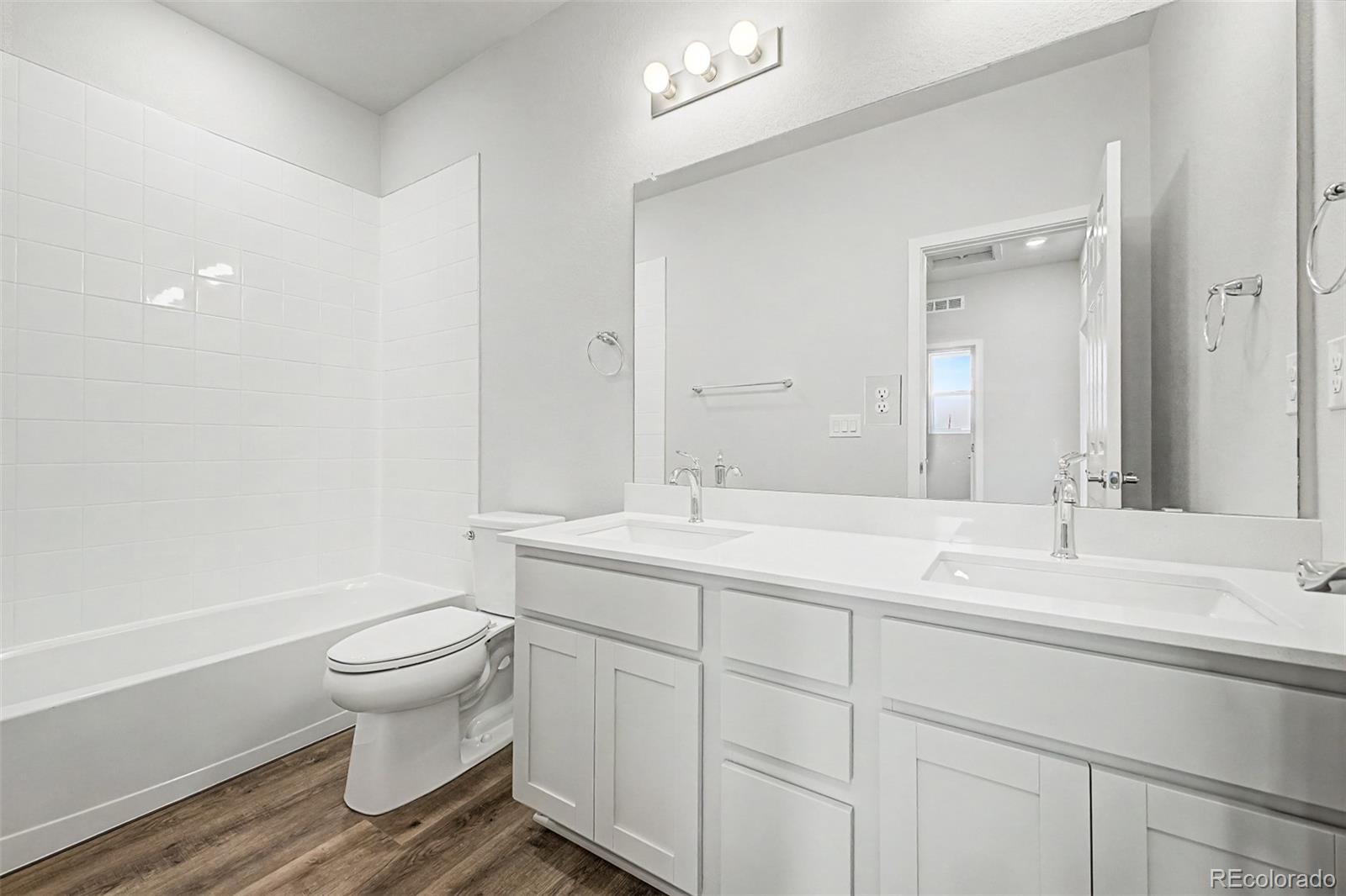 Bathroom with a tiled bathtub, toilet, and long white double-sink vanity.