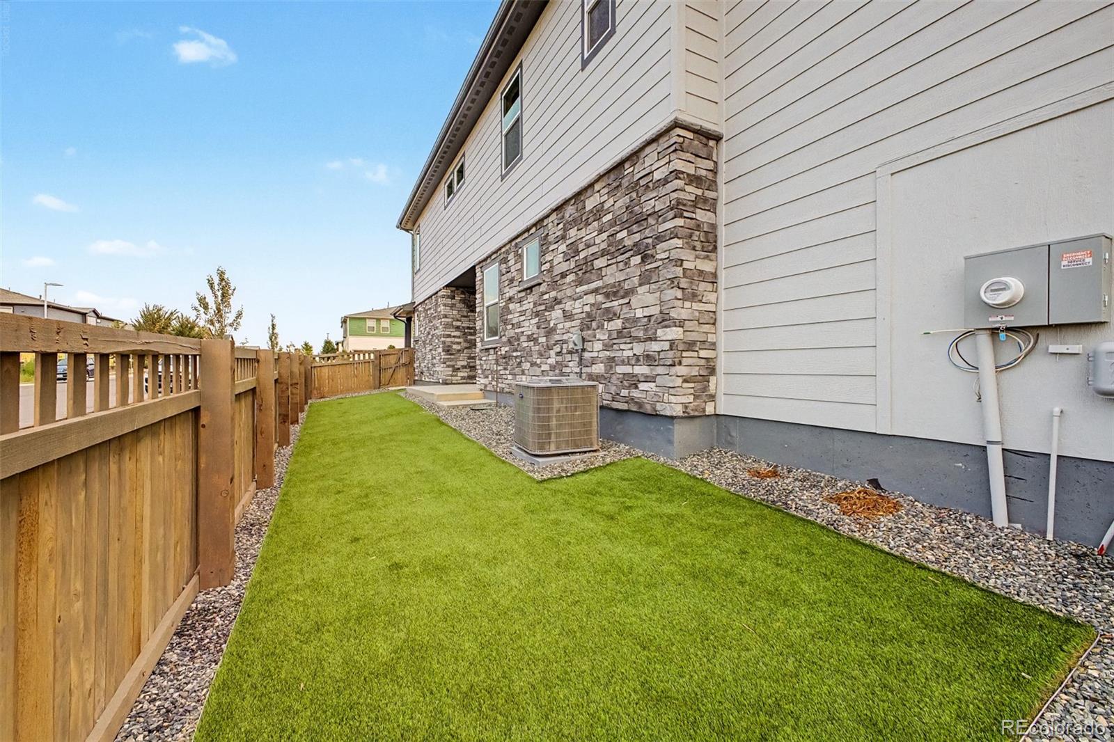 Side yard with a green lawn, wooden privacy fence, and stone-and-siding exterior.
