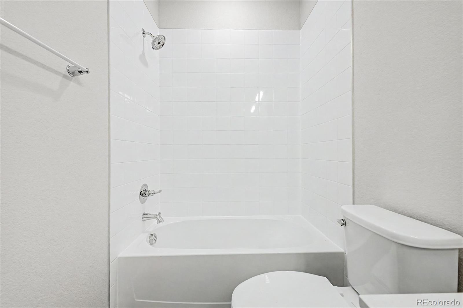 Bathroom with a white tiled tub-shower, chrome fixtures, and toilet.