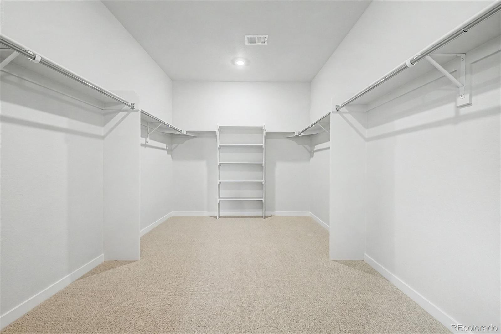 Walk-in closet with carpet, hanging rods on both sides, and built-in shelves at the back.