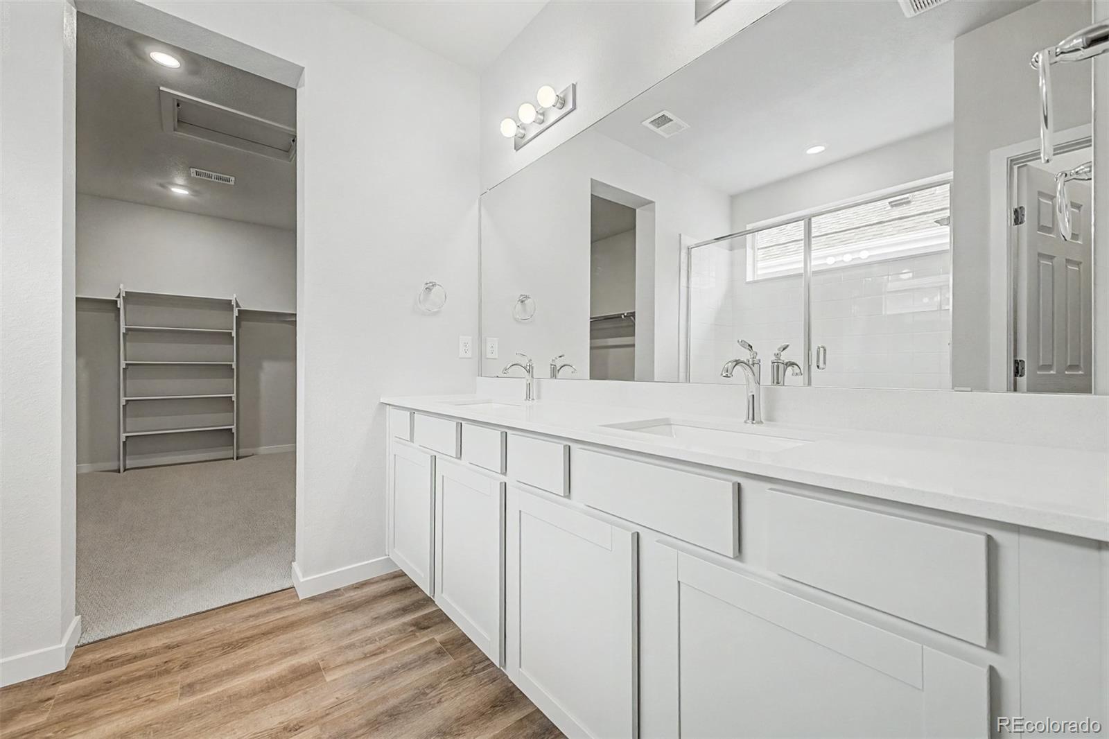 Primary bathroom with a long double vanity, mirrored glass shower, and adjoining walk-in closet.