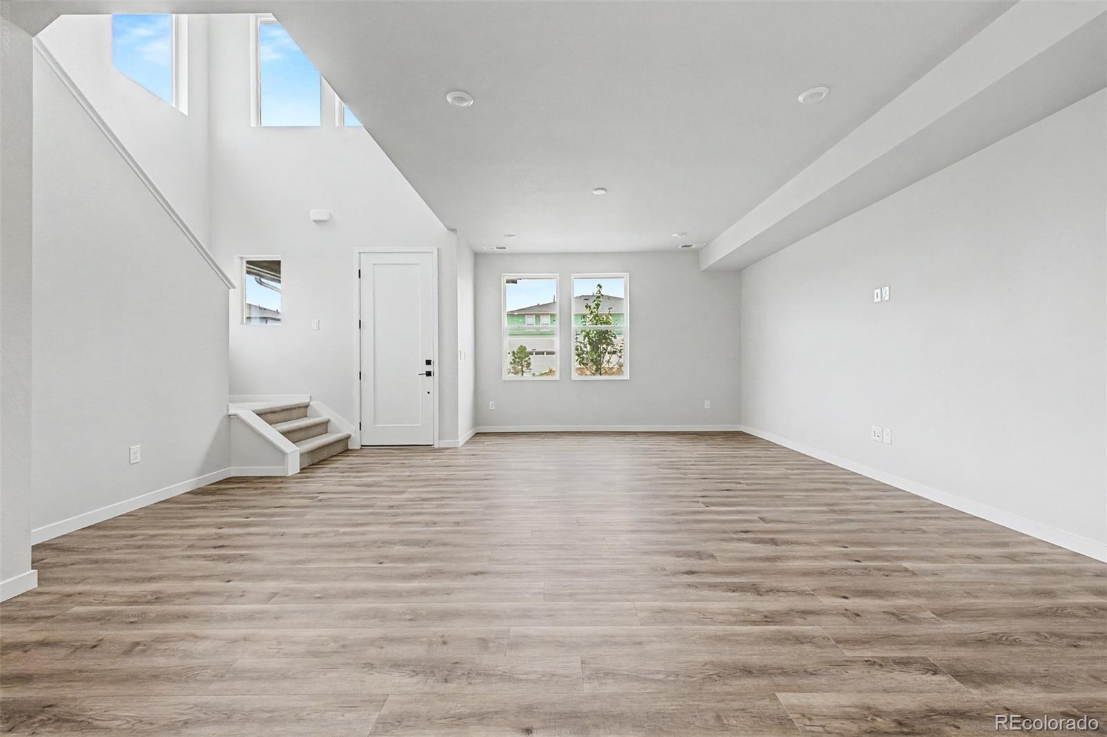 Vacant living area with wood-look floors, tall windows, and a short staircase.