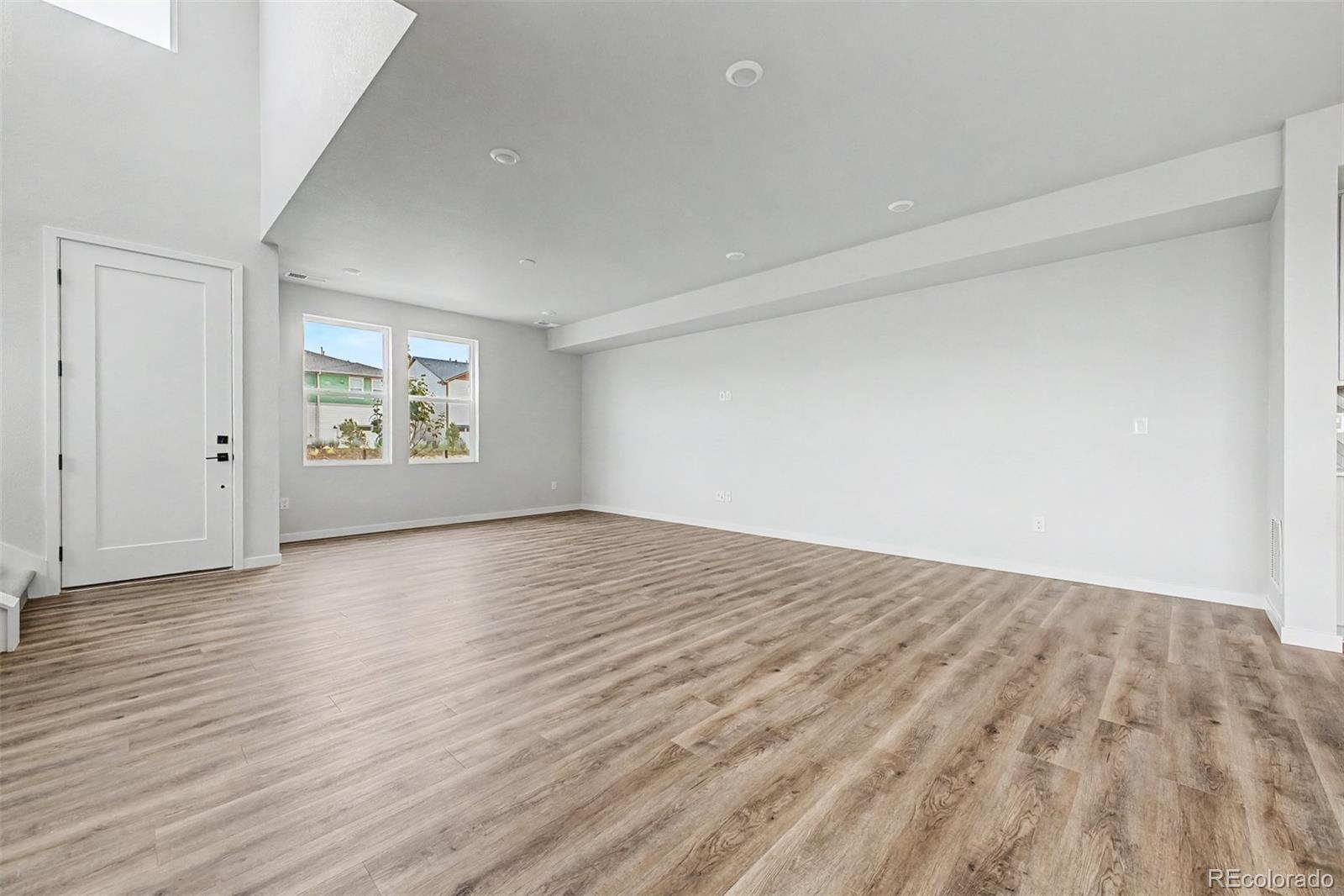 Empty living room with two windows, recessed lighting, and wood-look plank flooring.