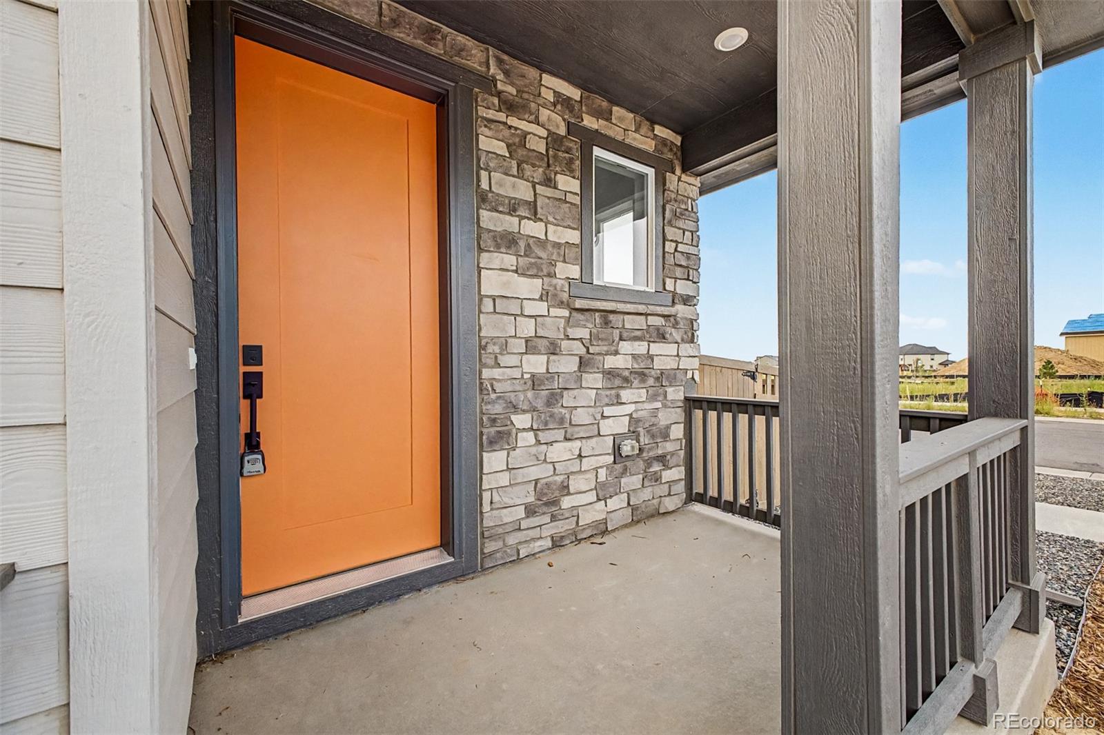 Covered entry porch with a bright orange front door, stone wall, and gray railing.