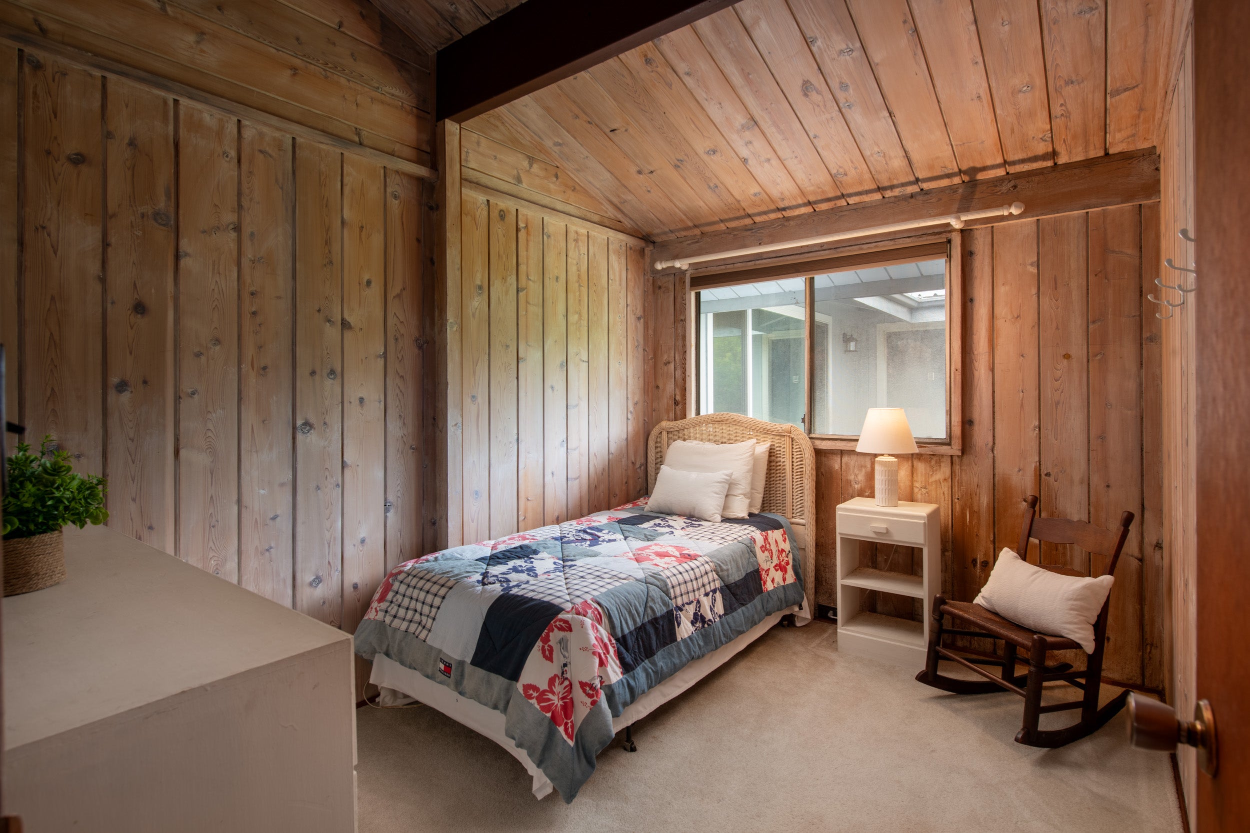 Wood-paneled bedroom with a patchwork-quilt bed and wooden rocking chair.