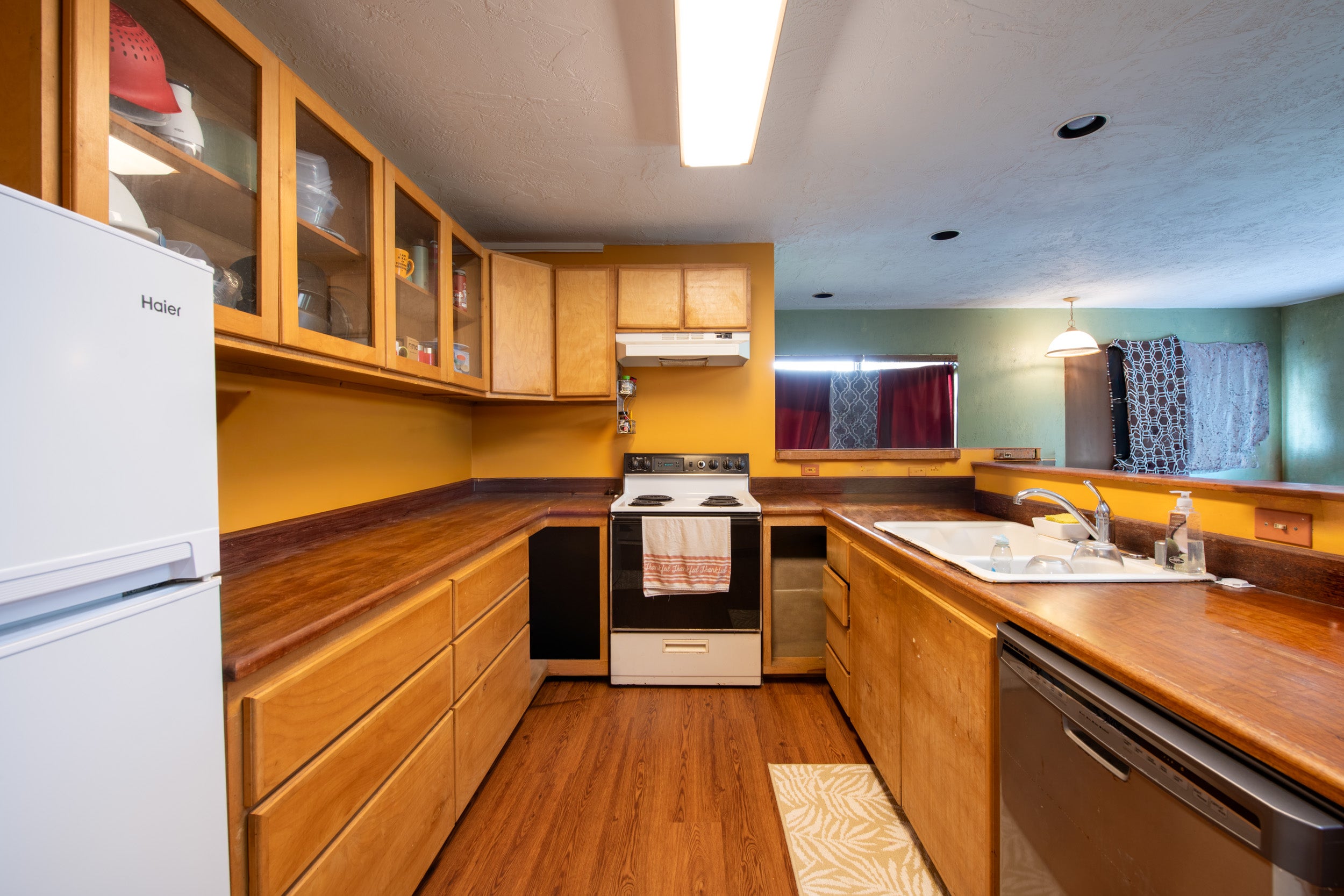 Kitchen with honey-colored wood cabinetry, dark countertops, a central stove, and a sink-side dishwasher.