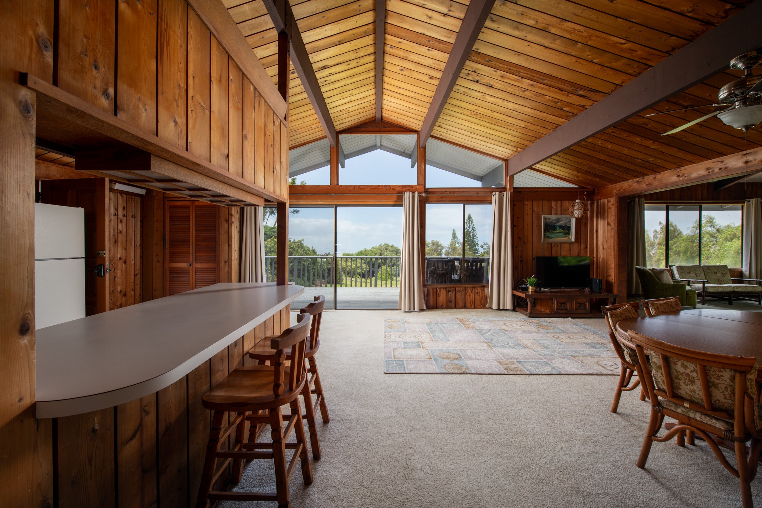 Open-plan living and dining room with a vaulted timber ceiling, breakfast bar, and sliding doors to a deck.