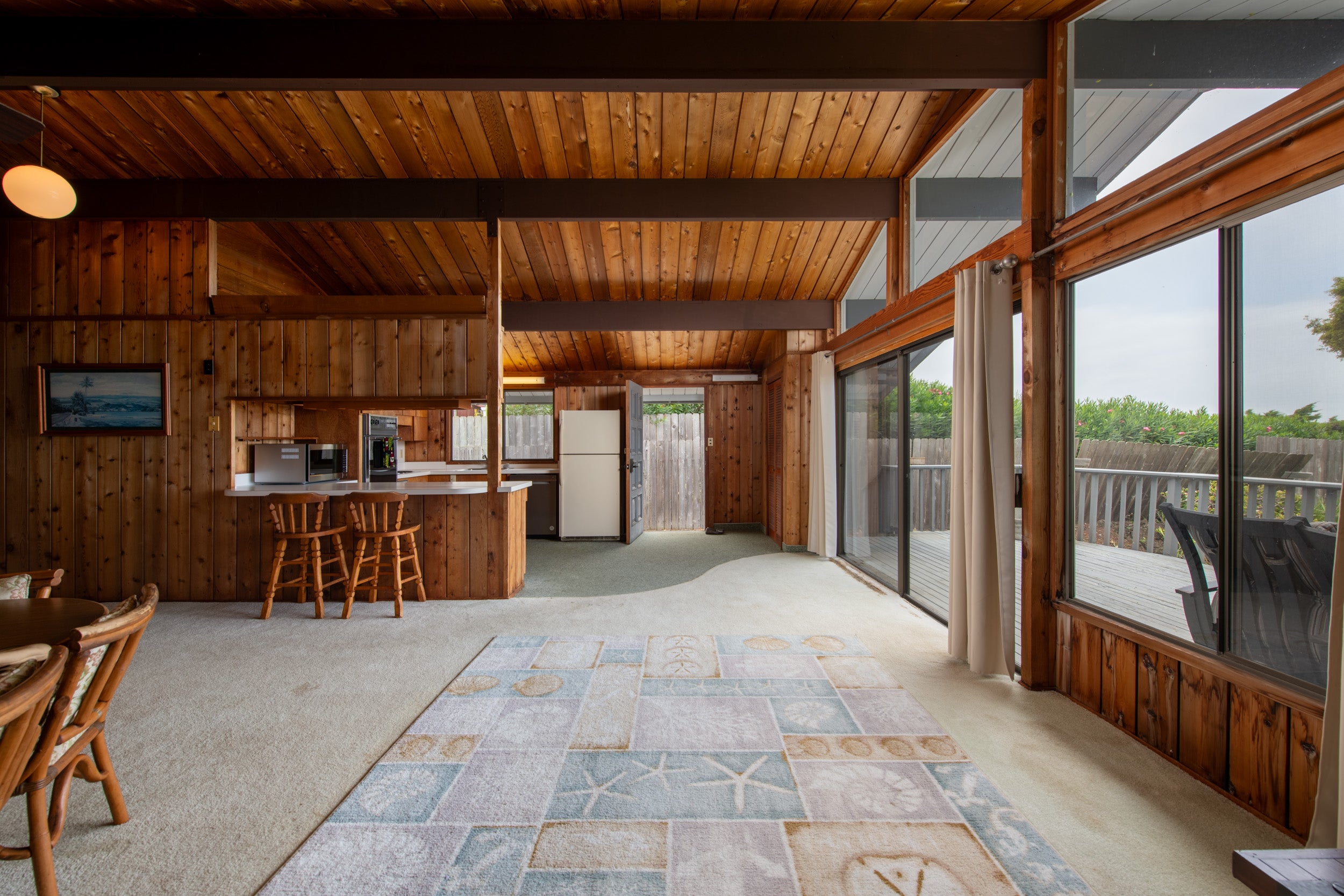 Wood-paneled living area with vaulted ceiling, breakfast bar, and sliding doors to a deck.
