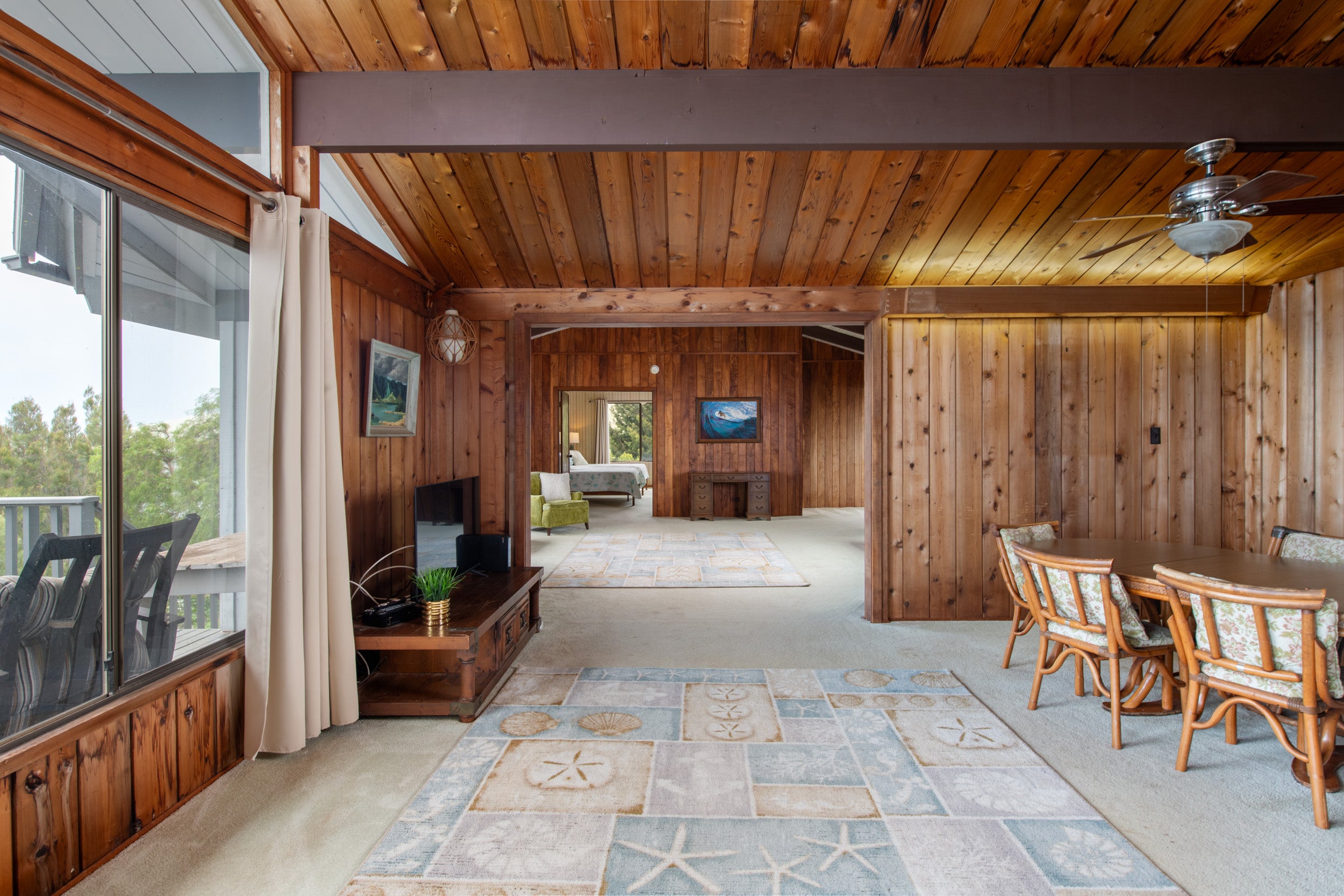 Open living and dining area with wood-paneled walls, high ceiling, and sliding glass doors to a deck.