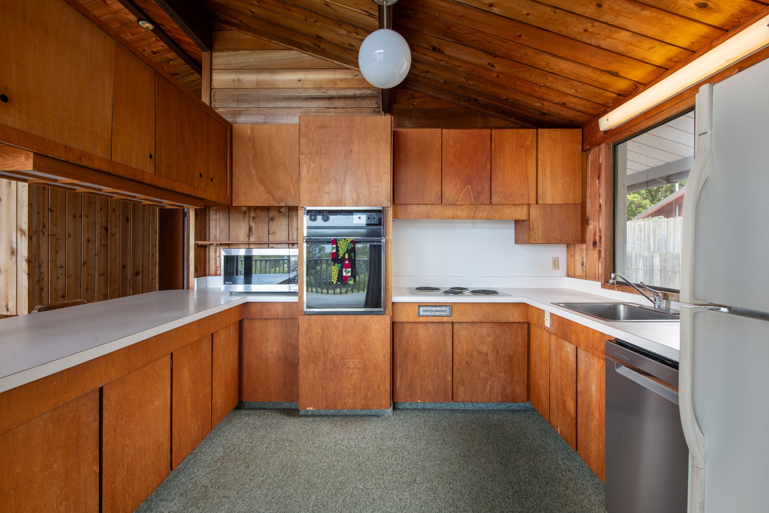Kitchen with extensive wood cabinetry, vaulted wood ceiling, white counters, and built-in appliances.