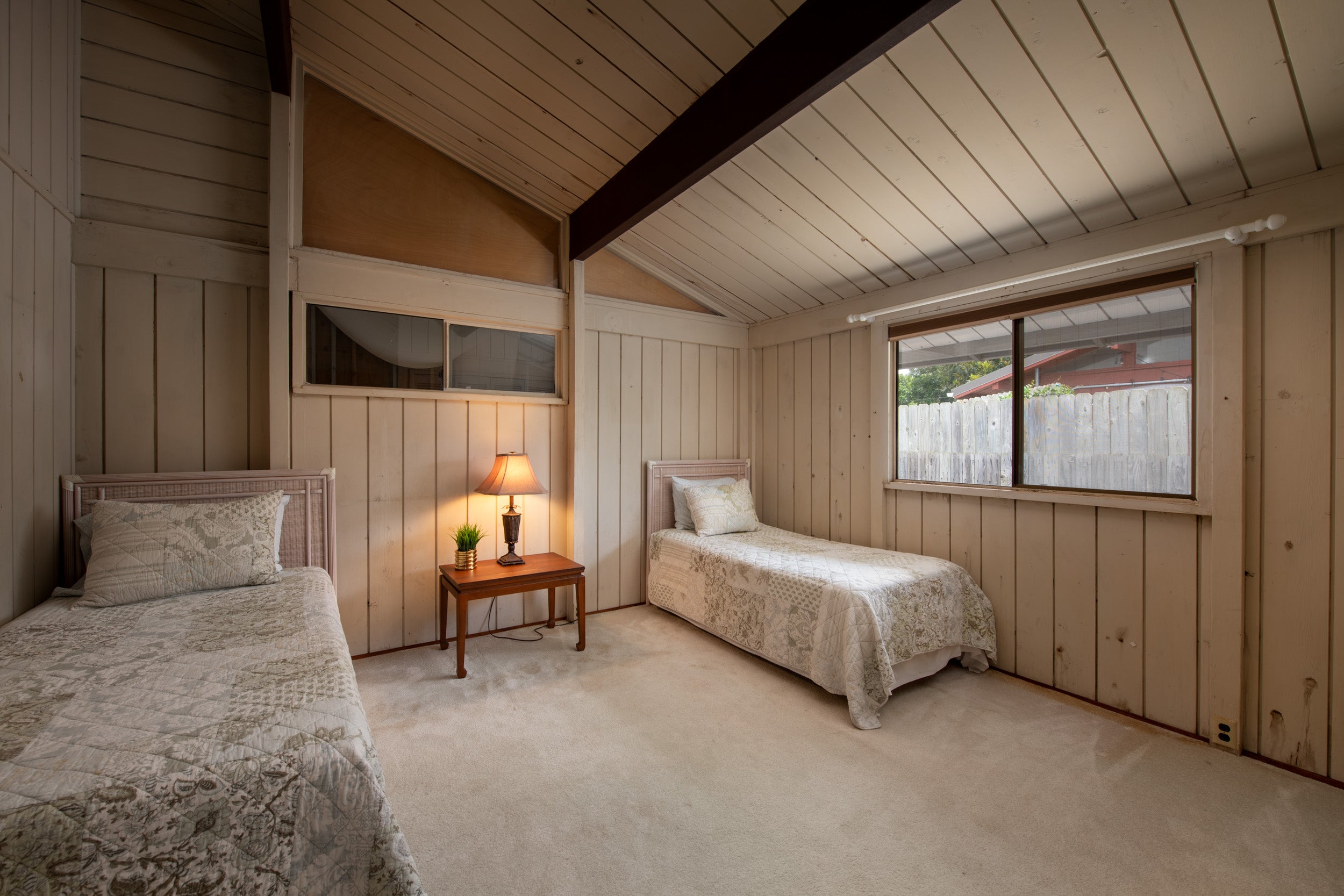 Bedroom with two twin beds, patterned quilts, wood-paneled walls, and a vaulted ceiling.