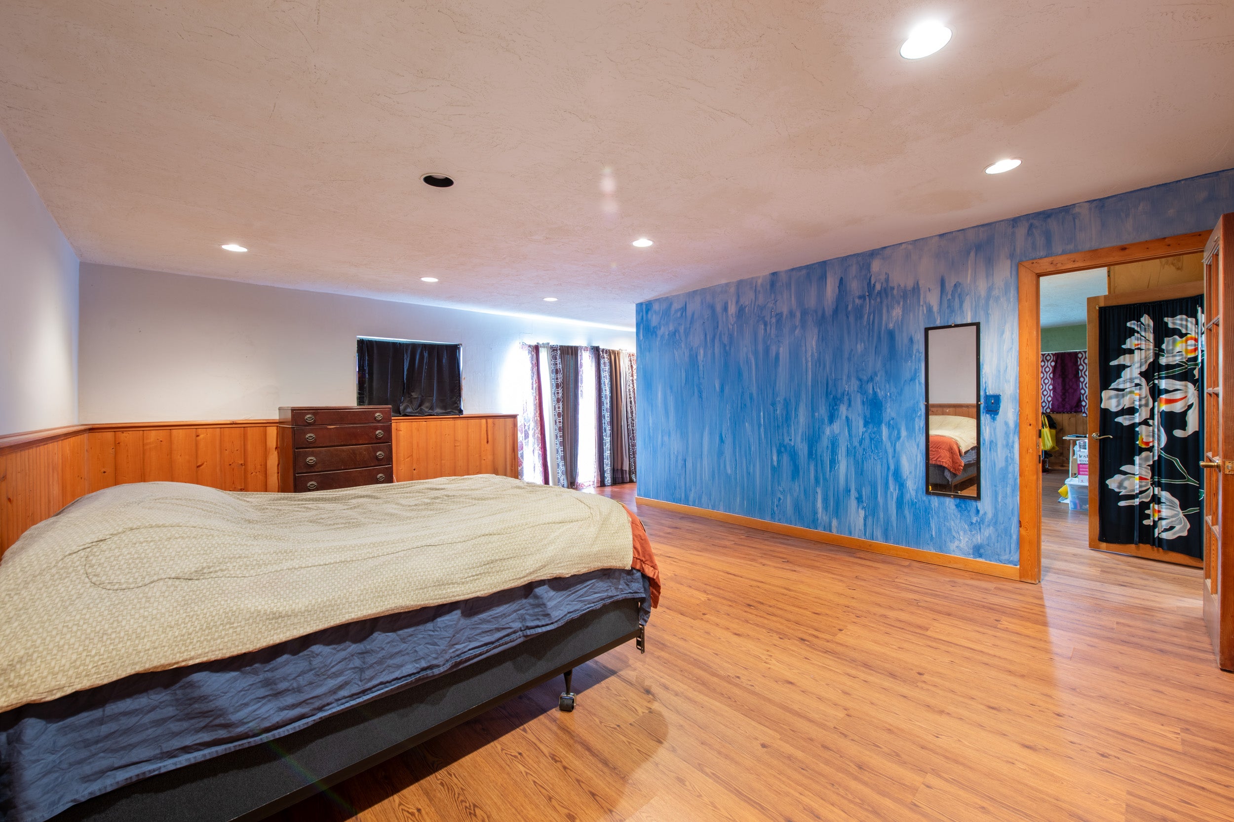 Bedroom with a vivid blue accent wall, wood wainscoting, and warm wood flooring.