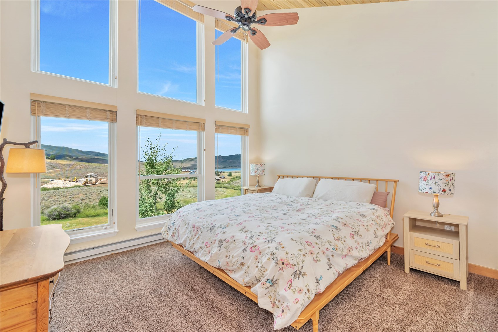 Furnished bedroom with a wooden bed and tall windows overlooking open countryside.