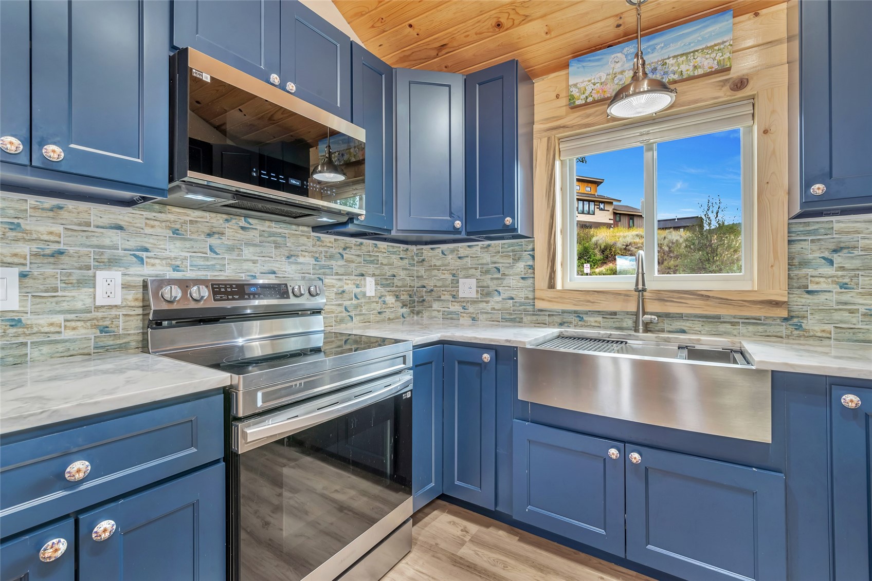 Kitchen with blue cabinets, stainless appliances, and a large sink beneath a window.