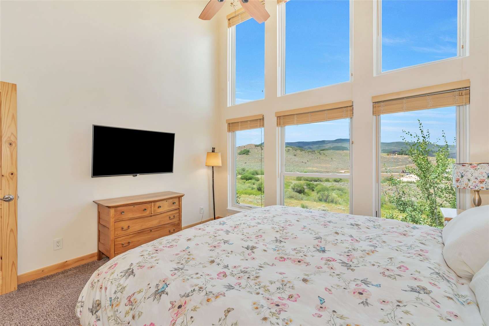 Bedroom with a floral bedspread and tall windows overlooking rolling hills.