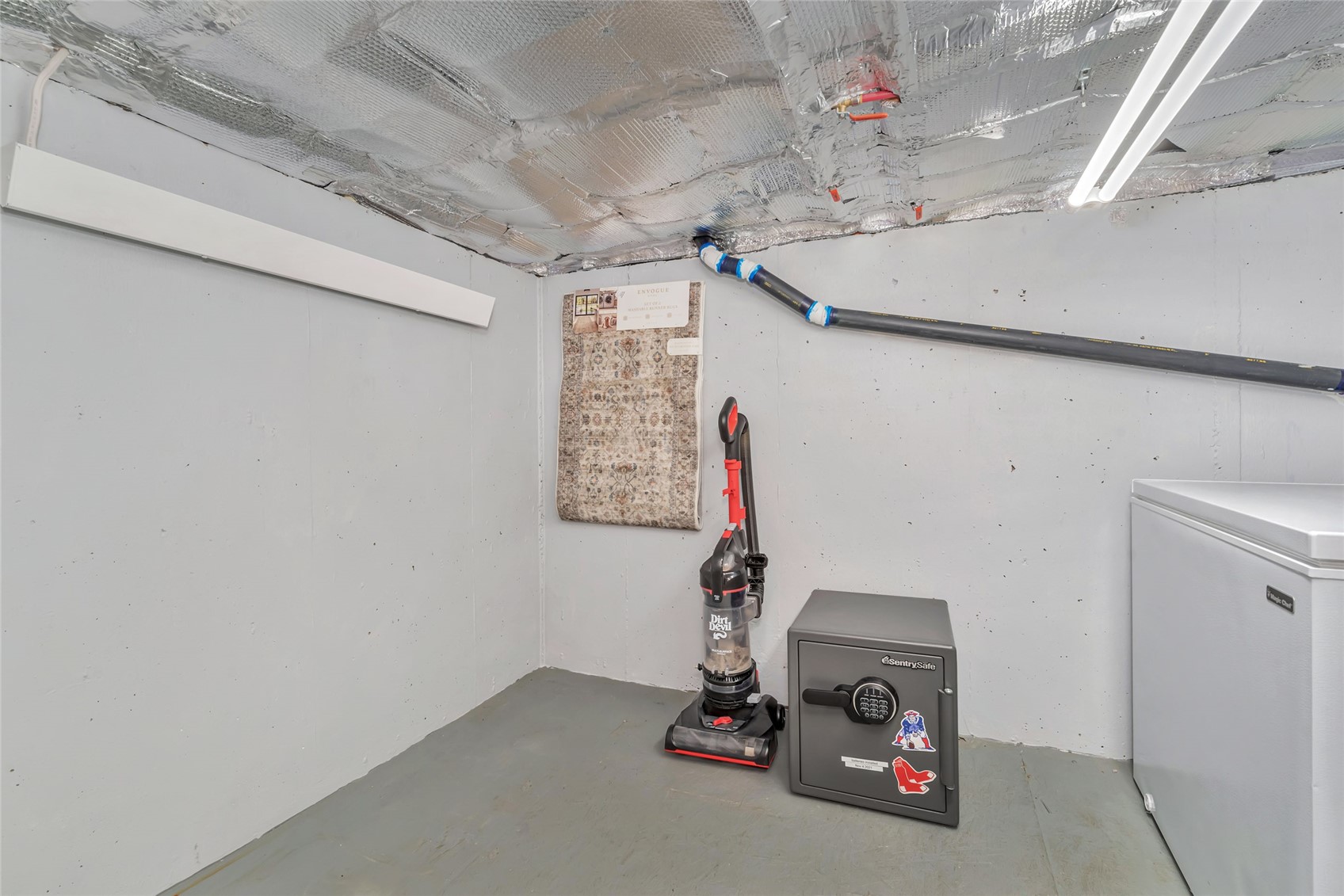 Basement storage room with an exposed insulated ceiling, vacuum, safe, and chest freezer.