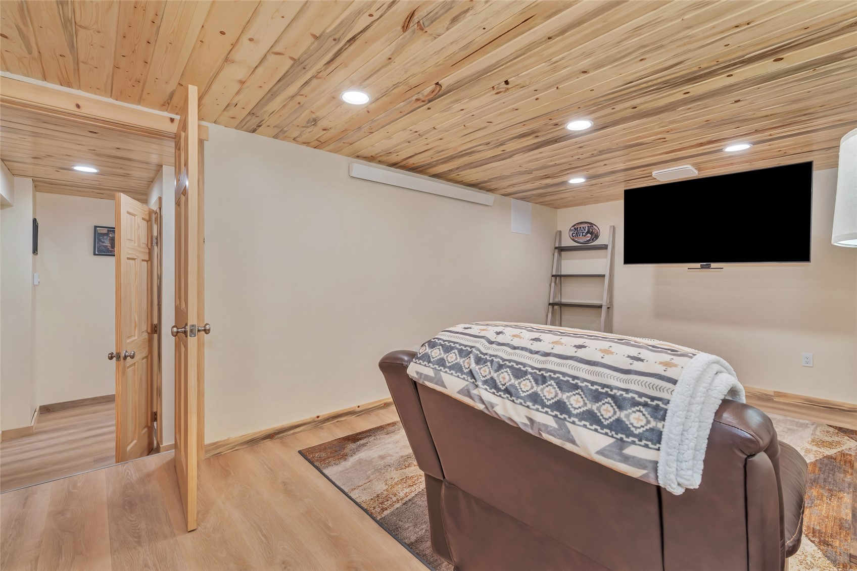 Media room with a wood-plank ceiling, wall-mounted television, and leather recliner.