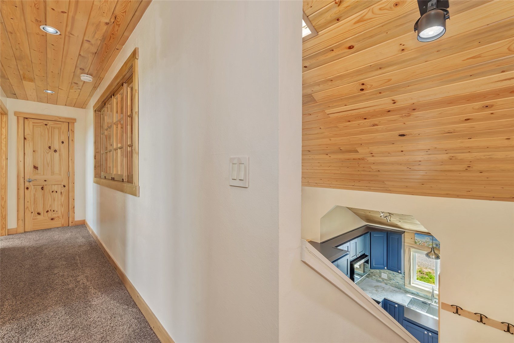 Carpeted hallway with a knotty-pine ceiling and a view down to a blue-cabinet kitchen.