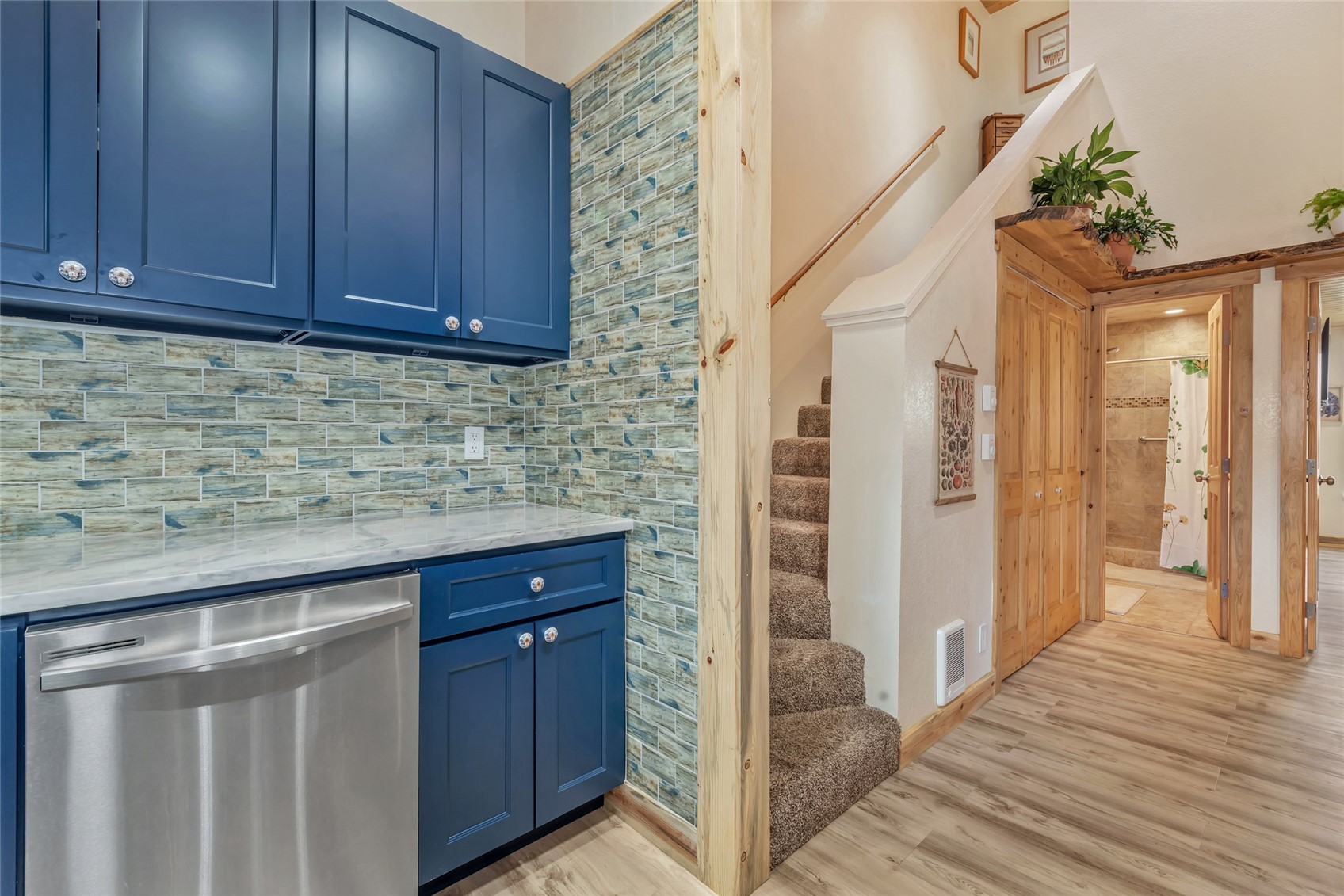Compact kitchen with navy cabinets and tiled backsplash beside a staircase and hallway.
