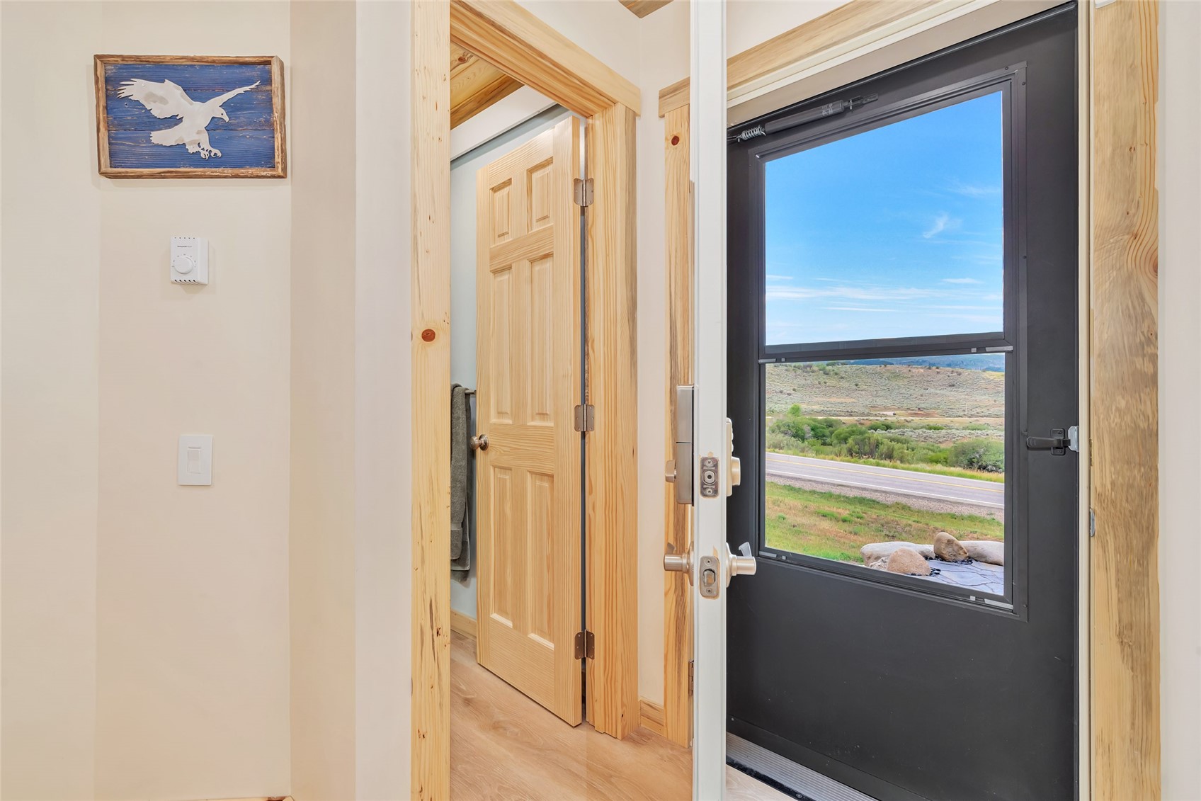 Entryway with natural wood trim and a dark windowed door overlooking a road and open landscape.