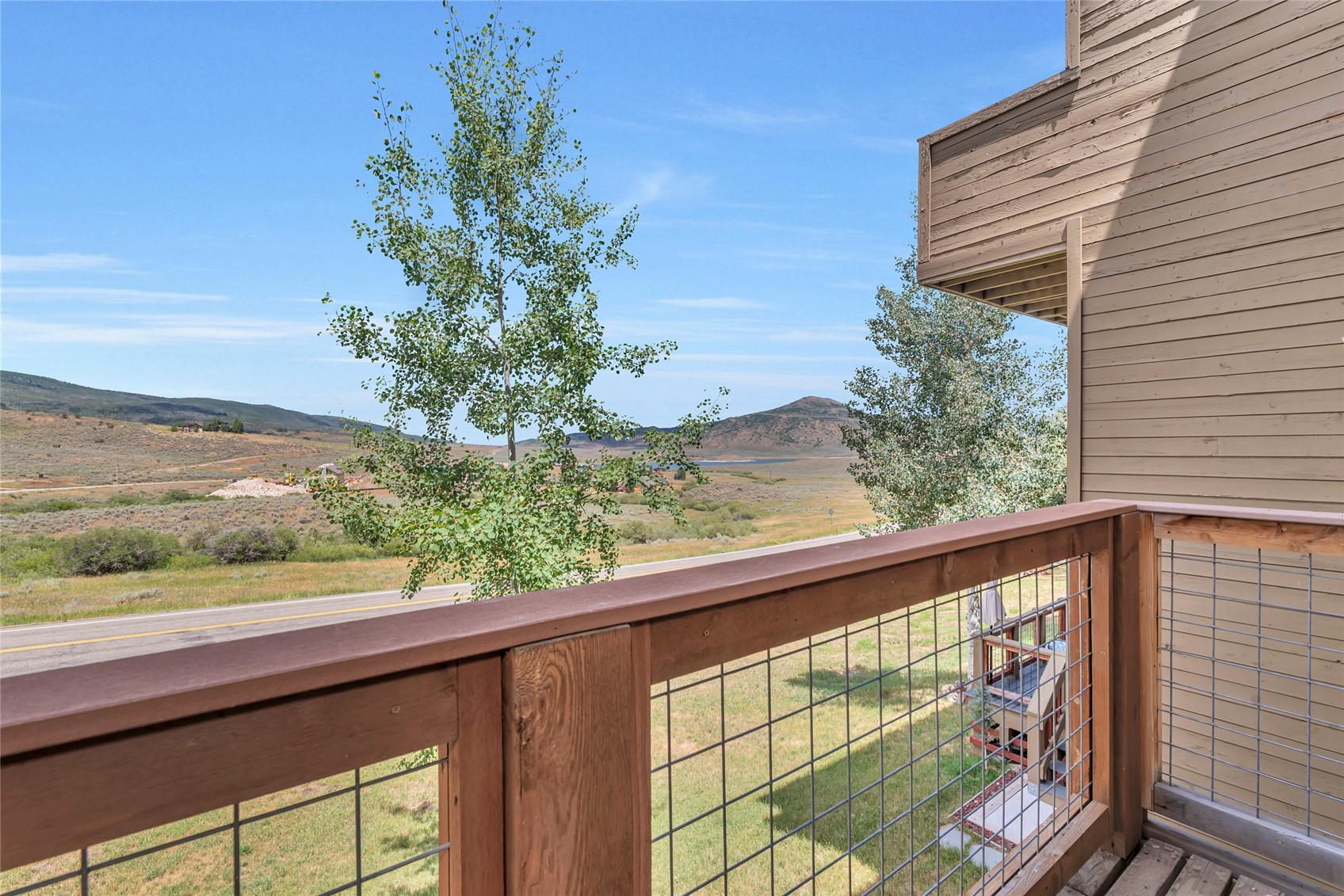 Wooden balcony overlooking a grassy valley, road, and distant mountains.