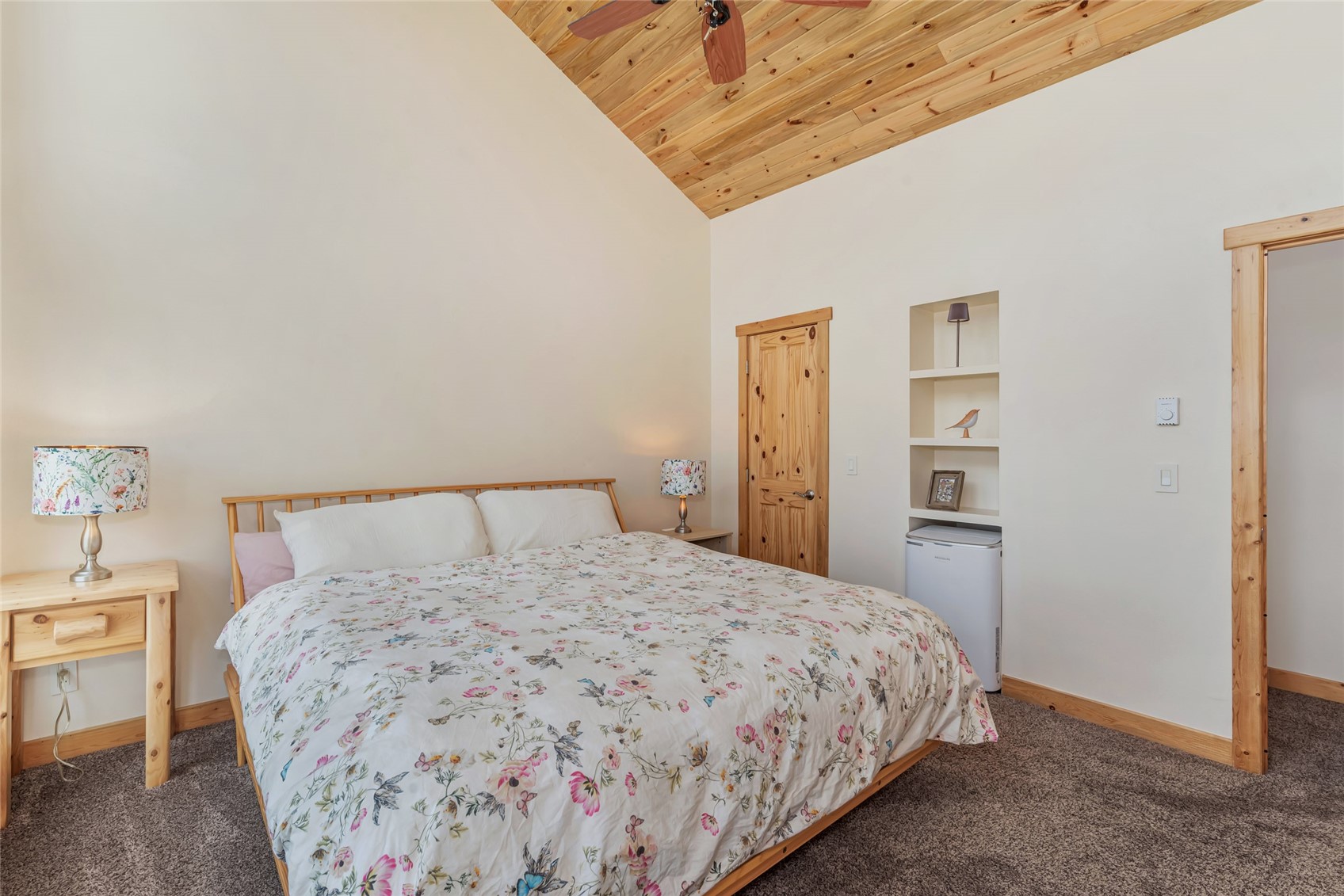 Bedroom with floral bedding, knotty pine details, and a vaulted wood ceiling.