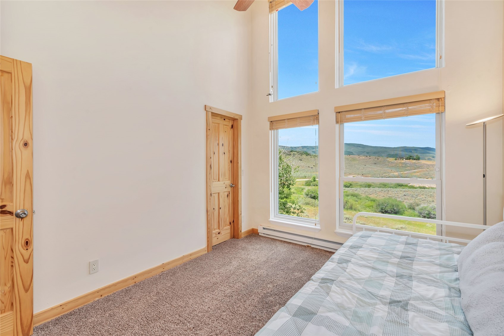 Bedroom with tall windows overlooking open scrubland and rolling hills.