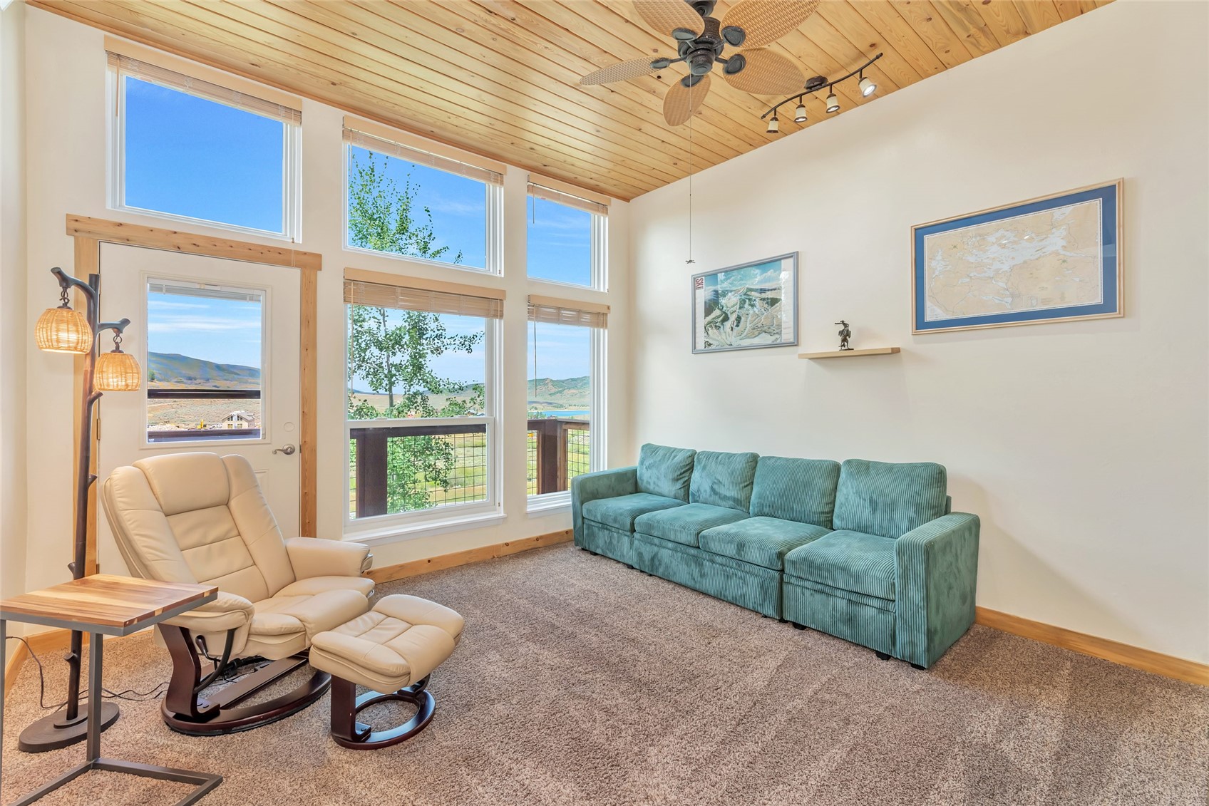 Living room with a vaulted wood ceiling, teal sofa, and tall windows overlooking hills.