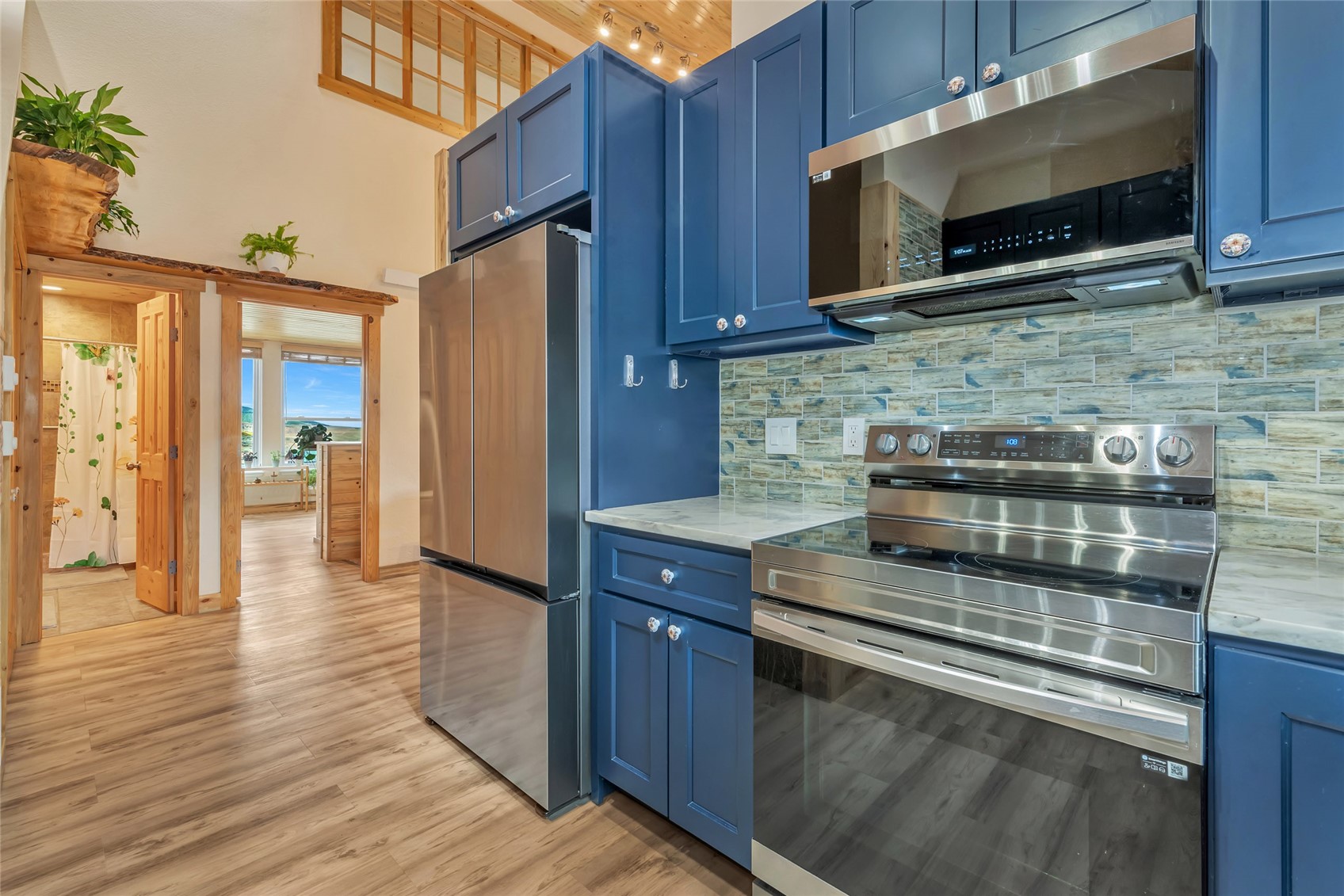 Kitchen with blue cabinets, stainless steel appliances, and a multicolored tile backsplash beneath a wood ceiling.