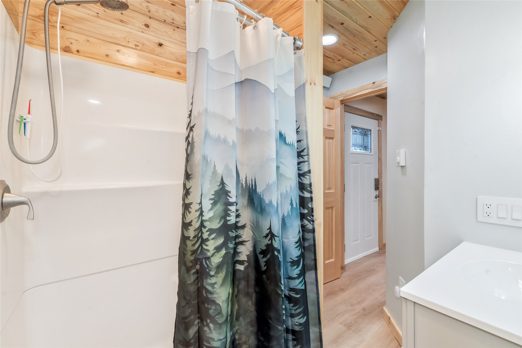 Bathroom with a forest-print shower curtain and wood-plank ceiling.