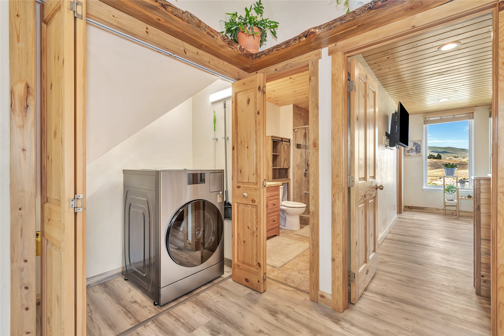 Laundry area with a stainless washer beside a wood-trimmed bathroom and hallway window.
