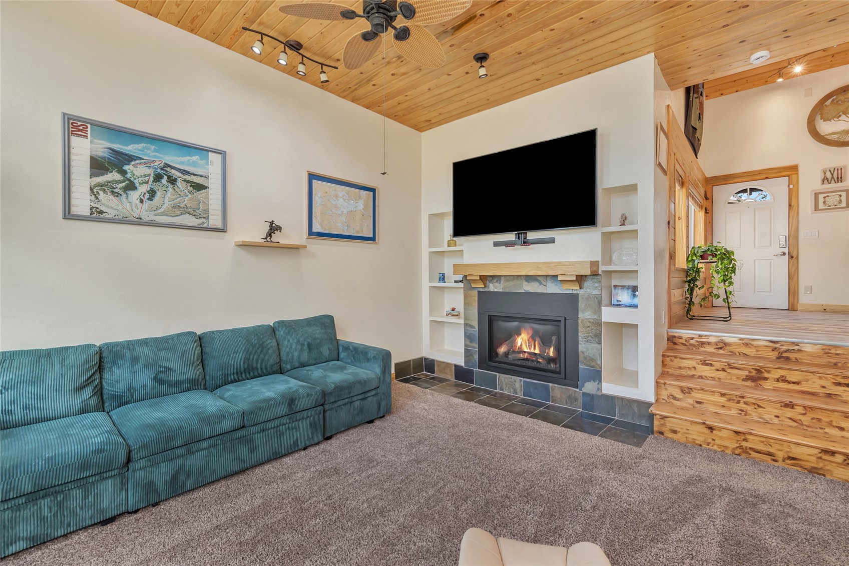 Living room with a teal sectional, stone fireplace, built-in shelves, and vaulted wood ceiling.