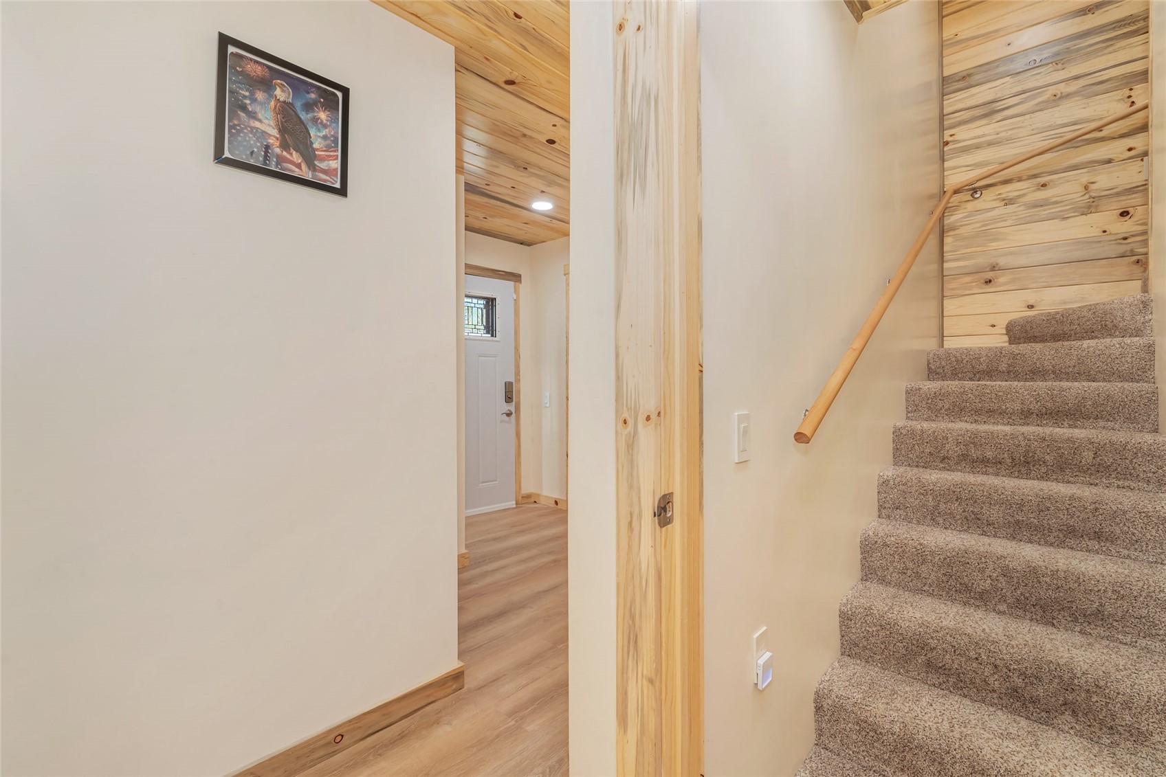 Entryway with carpeted stairs, a wood handrail, and a hallway leading to the front door.