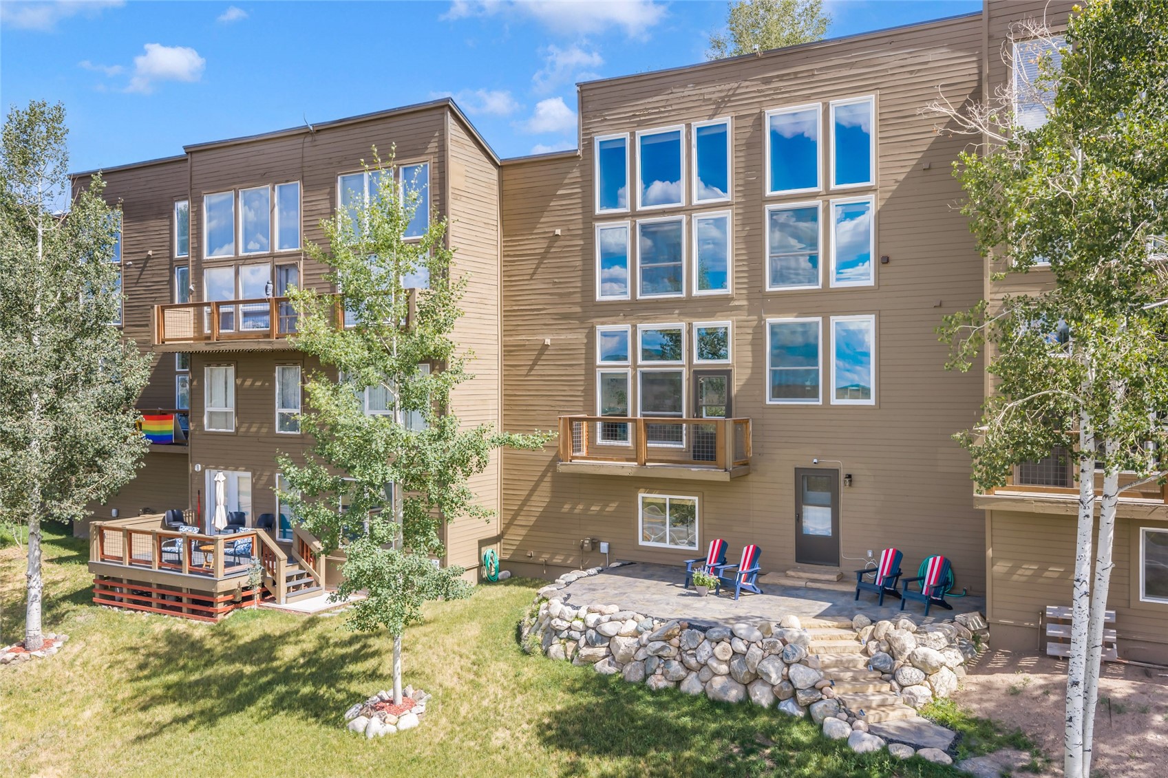 Multi-story brown residential building with private decks and a stone-edged patio.