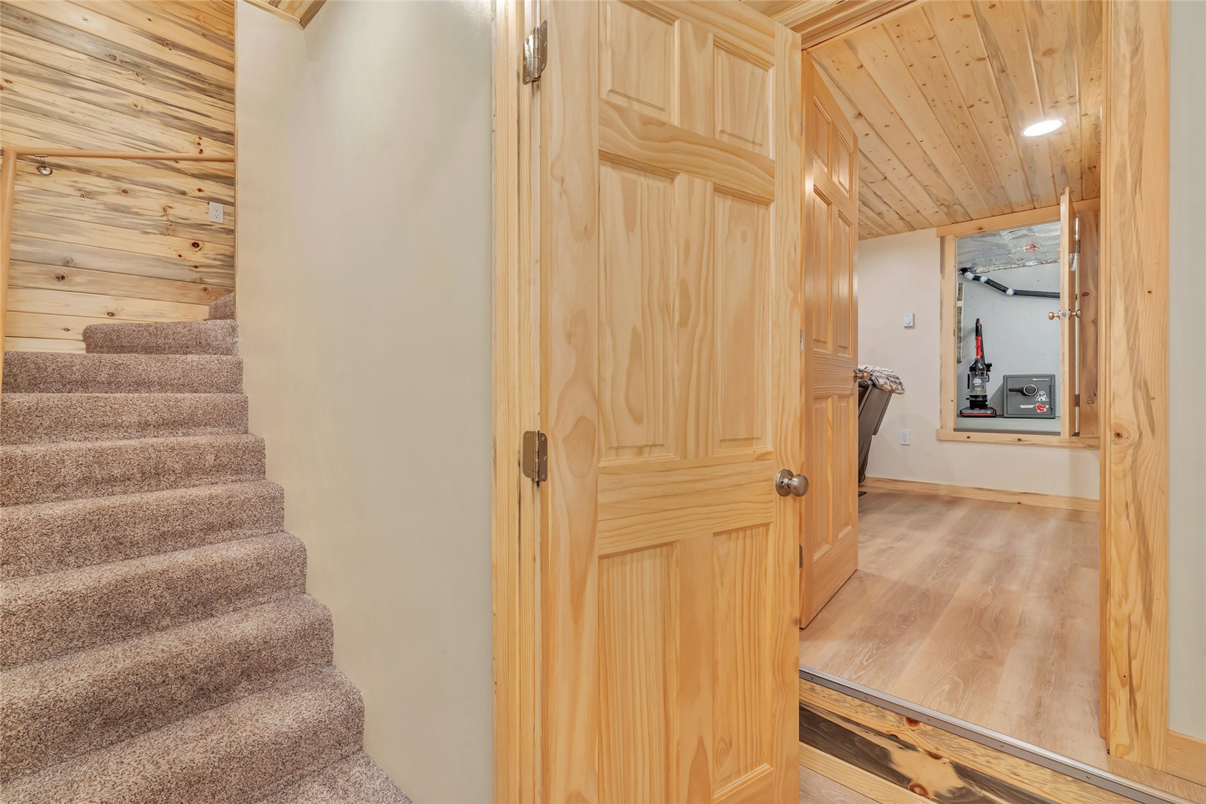 Hallway with carpeted stairs, an open pine door, and a vaulted wood-plank ceiling.