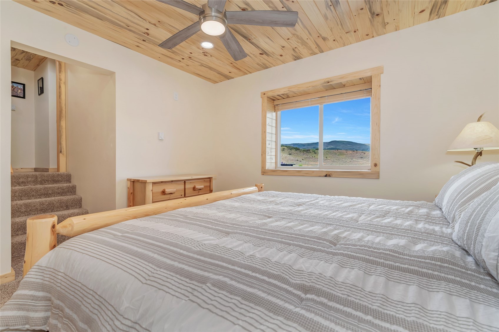 Bedroom with a pine-plank vaulted ceiling and a window overlooking rolling hills.