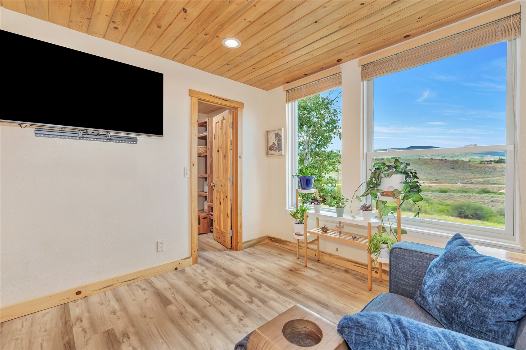 Living room with a wood ceiling, blue sofa, and large windows overlooking open countryside.