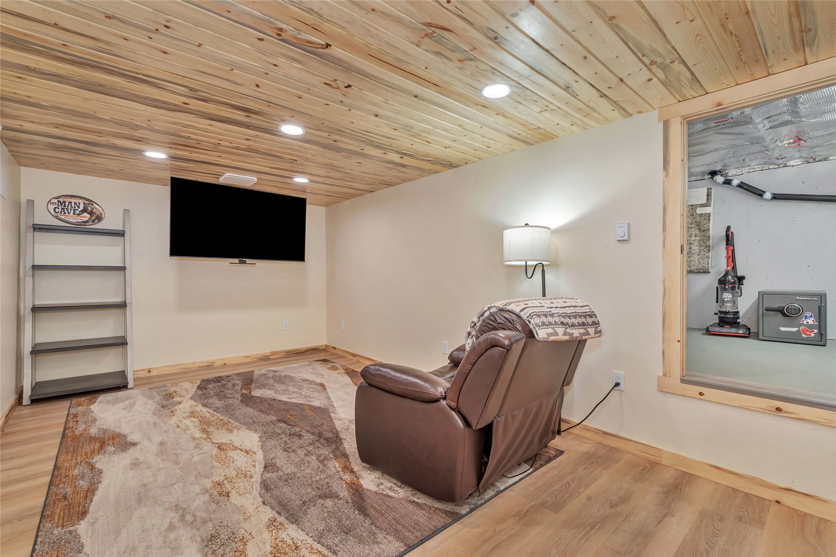 Furnished media room with a wood-plank ceiling, wall-mounted TV, and leather recliner.
