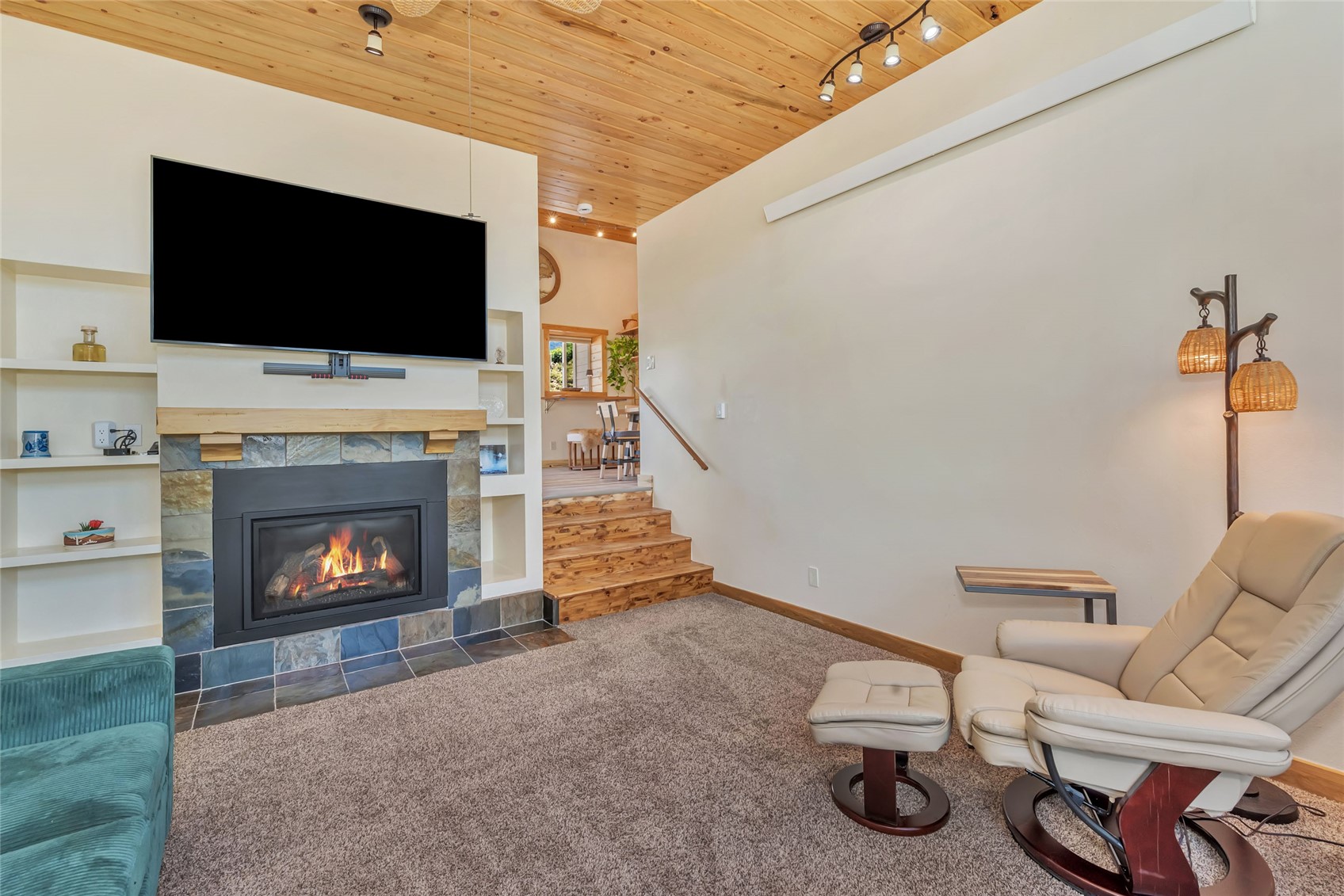 Living room with a slate fireplace, mounted TV, wood ceiling, and steps to the dining area.