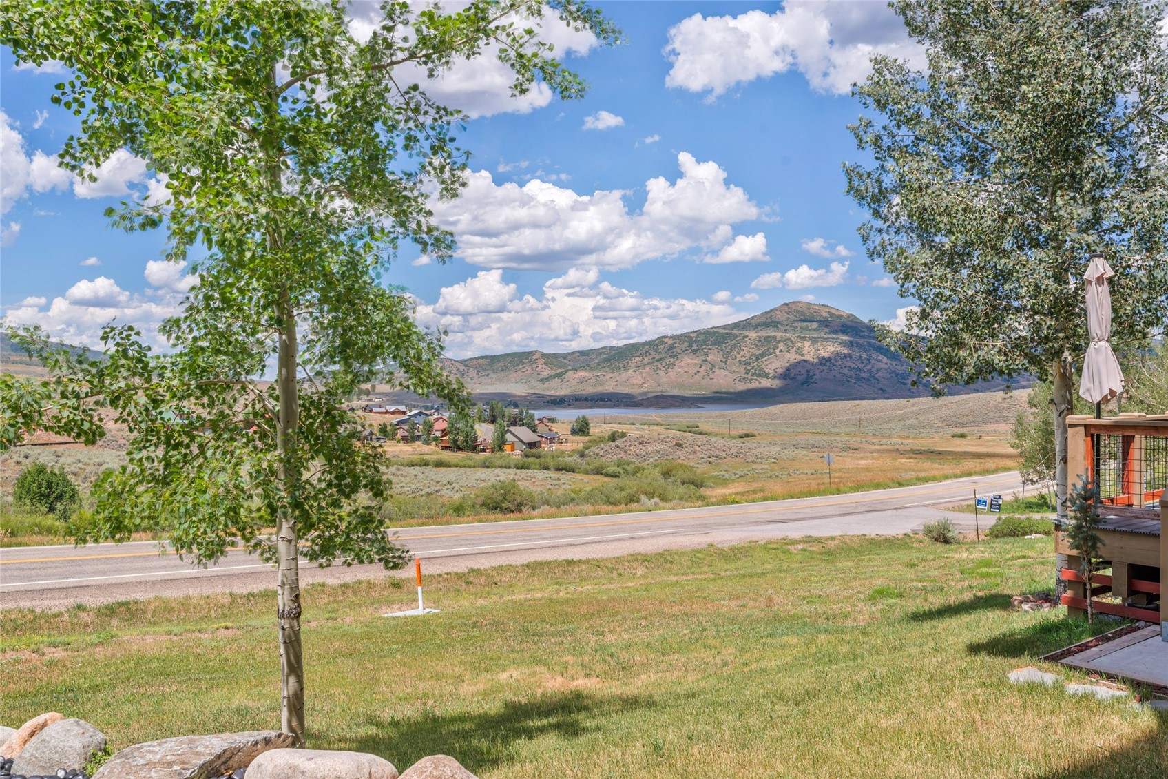 Yard and deck overlook a road, lakeside homes, and mountain slopes.