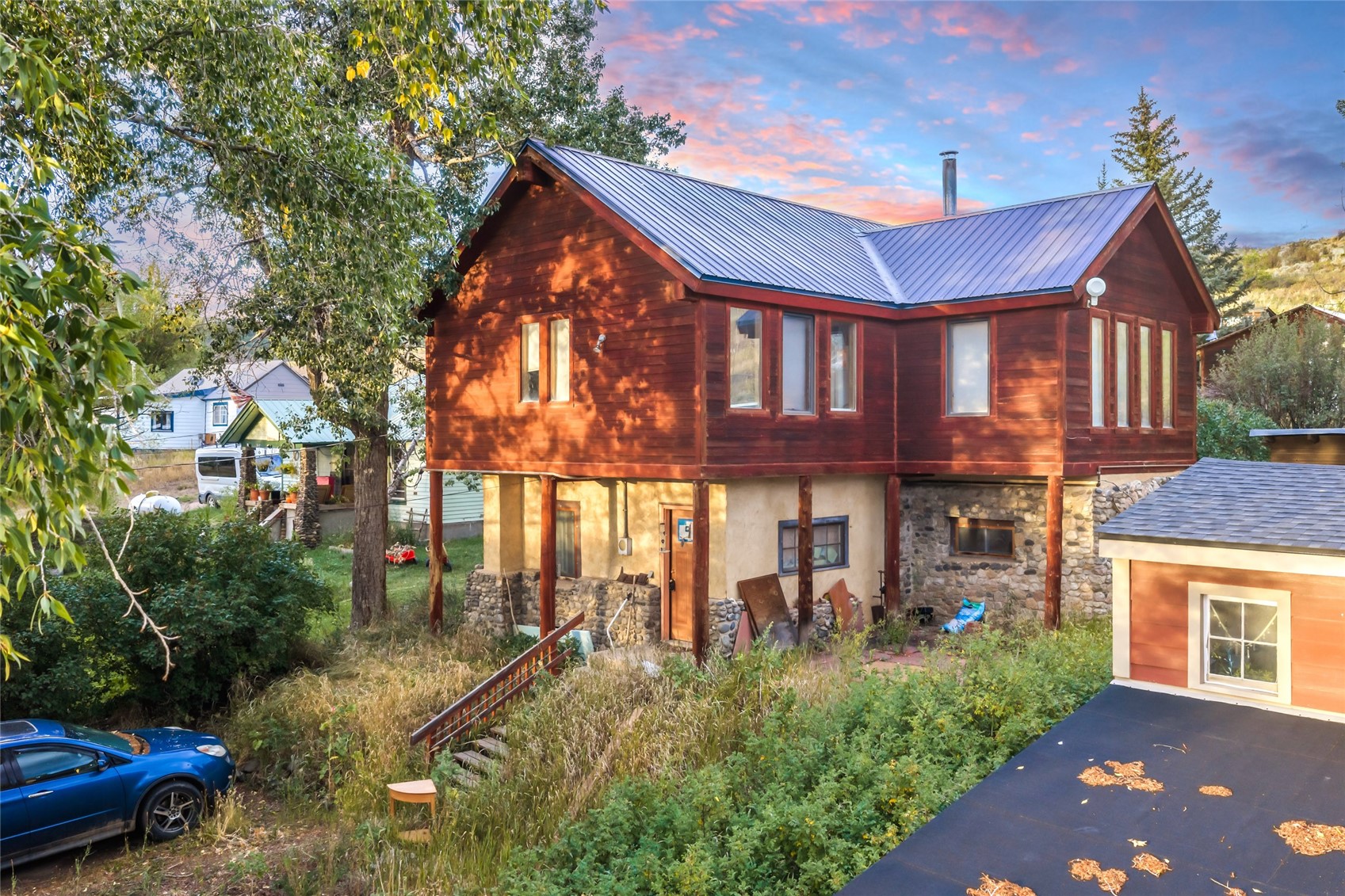 Raised wood house with a silver metal roof and stone lower level in warm evening light.