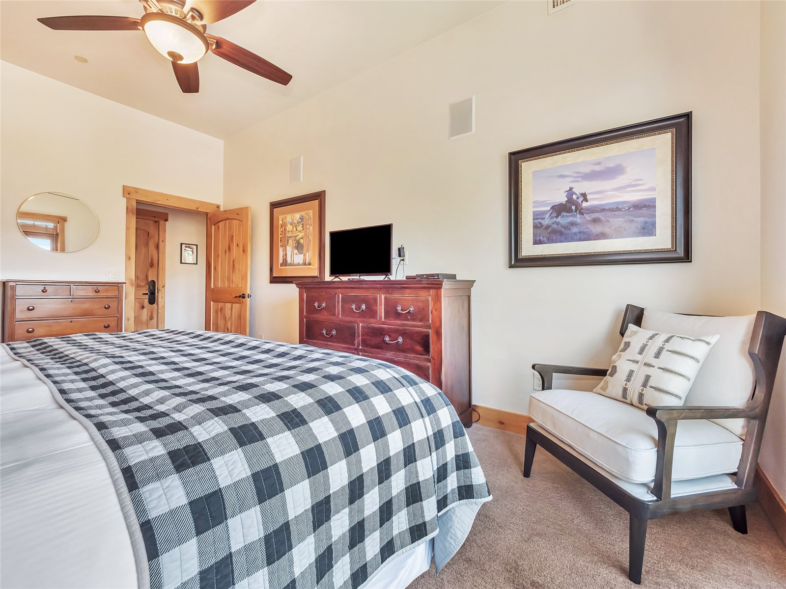 Bedroom with a black-and-white quilted bed, wooden dresser, ceiling fan, and cushioned armchair.