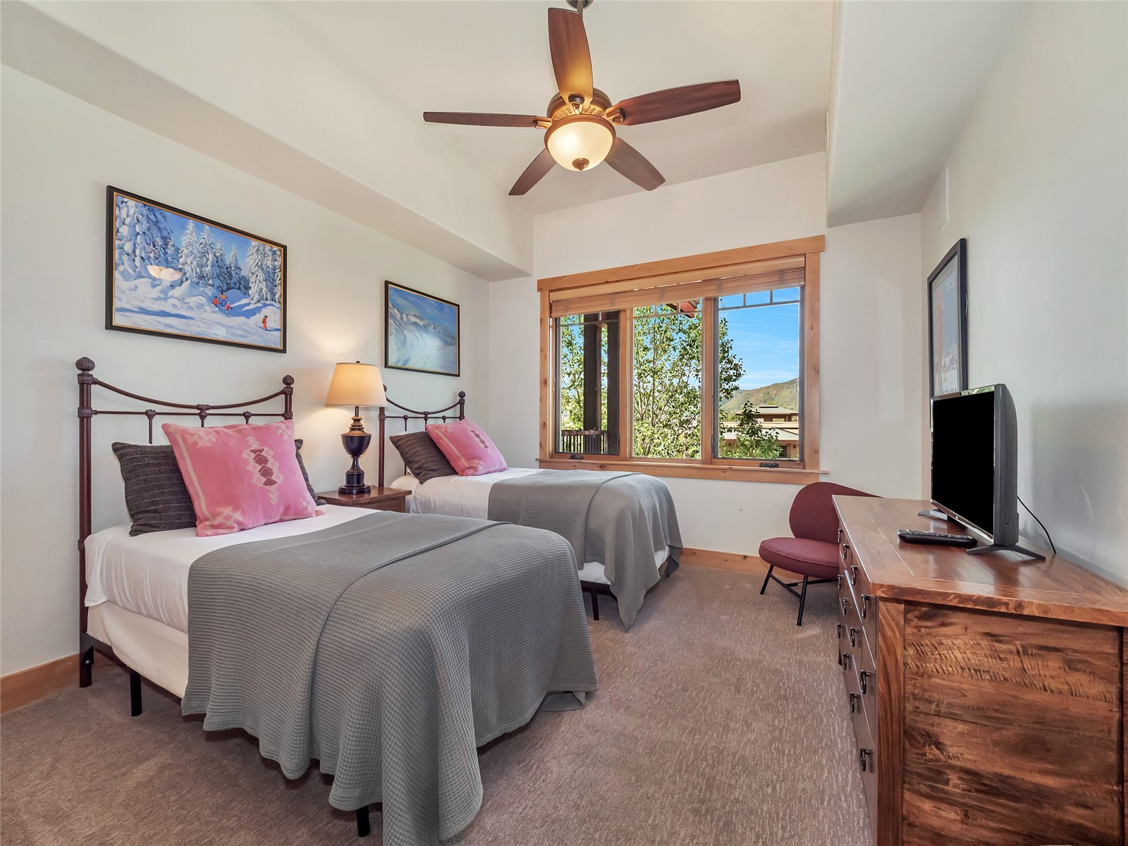 Furnished bedroom with two twin beds and a large window overlooking trees and distant hills.