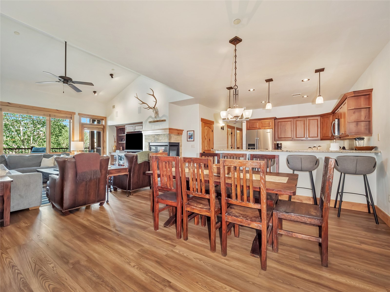 Open-plan dining and living area with a wooden table, stone fireplace, and vaulted ceiling.