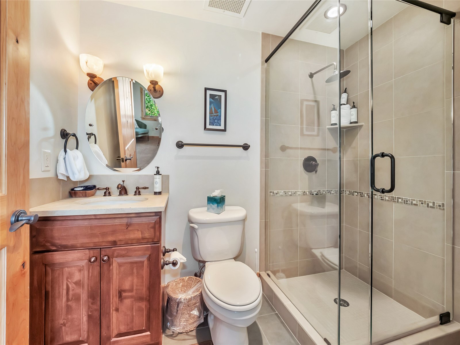 Bathroom with a wood vanity, oval mirror, and glass-enclosed tiled shower.