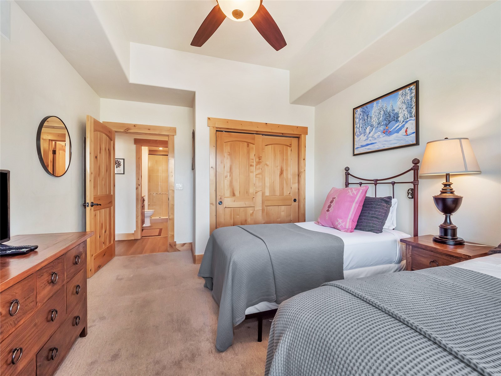 Bedroom with two gray-covered beds, wooden furnishings, and an open doorway to the ensuite bathroom.