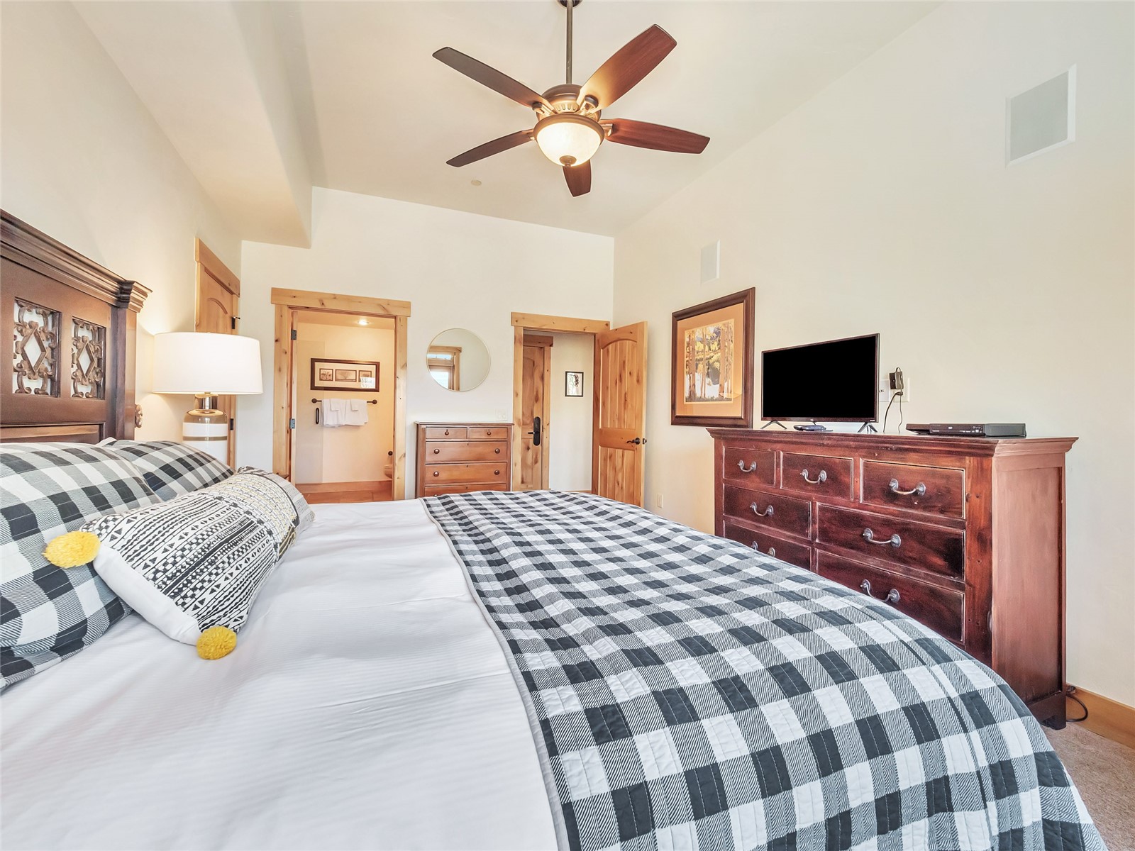 Furnished bedroom with a black-and-white patchwork quilt, wooden dresser, television, and ceiling fan.