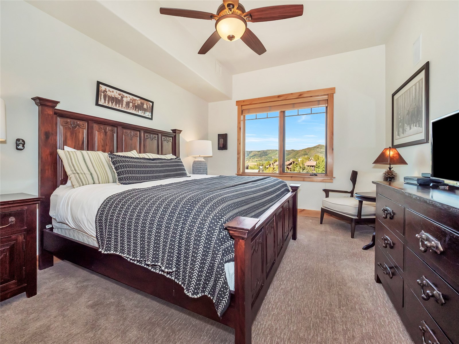Furnished bedroom with a carved wood bed and mountain views through a large window.